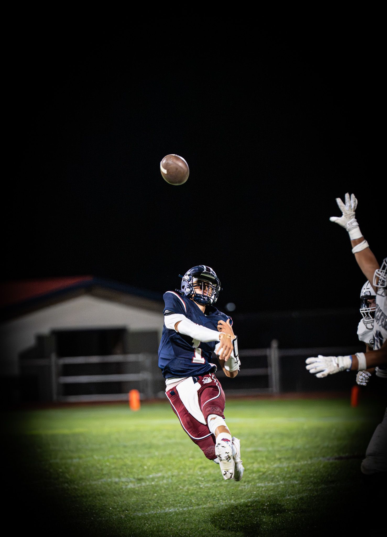 Football player makes diving catch attempt for ball during night game on grass field.