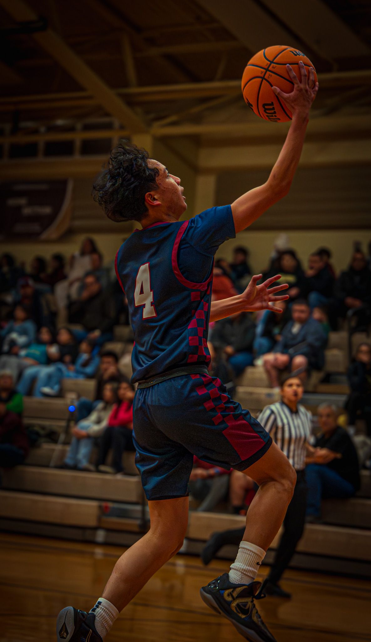 Basketball player in blue jersey leaps high for a layup during an indoor game.