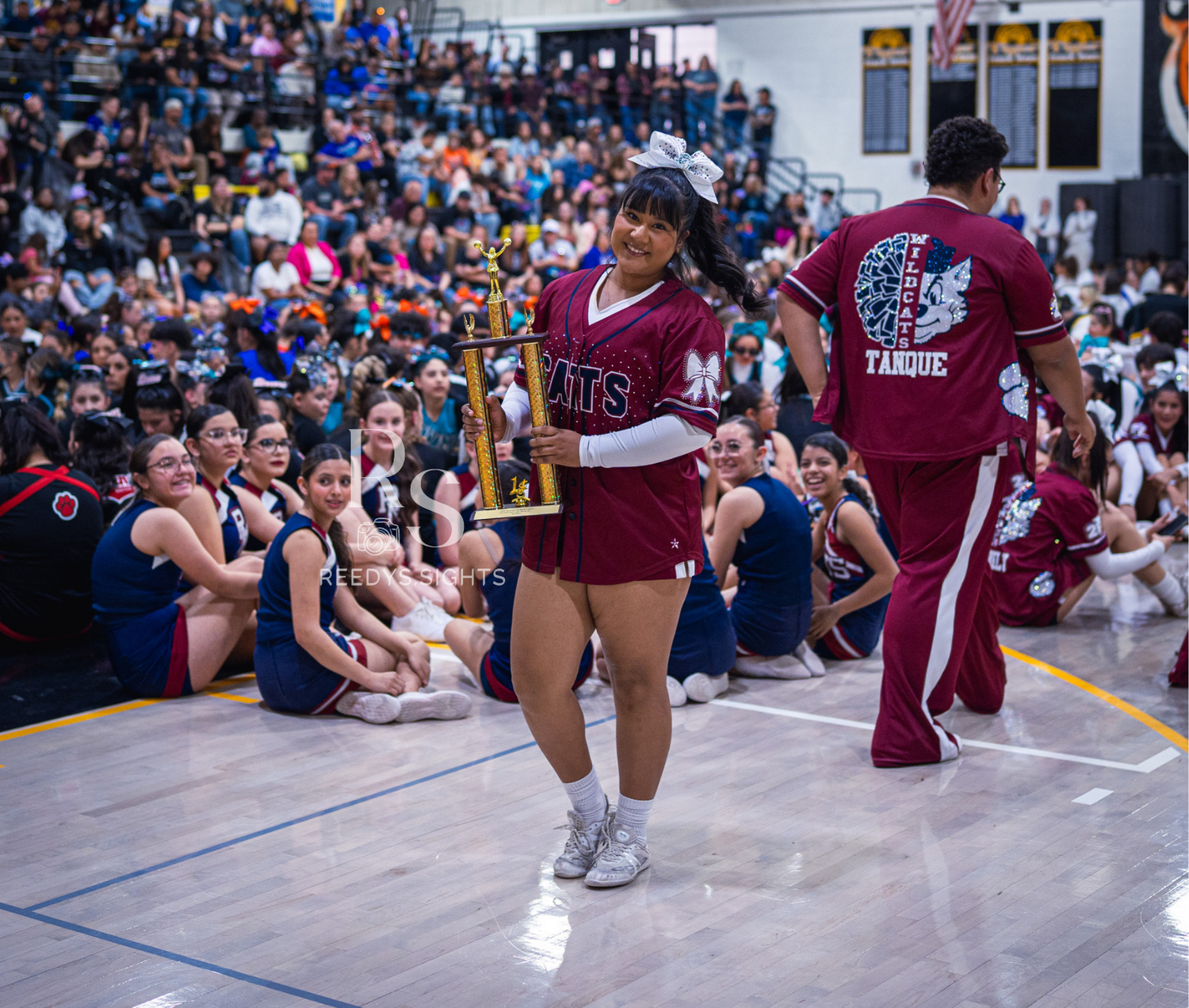 Cheerleaders in maroon uniforms execute synchronized kneeling poses during a competition routine.