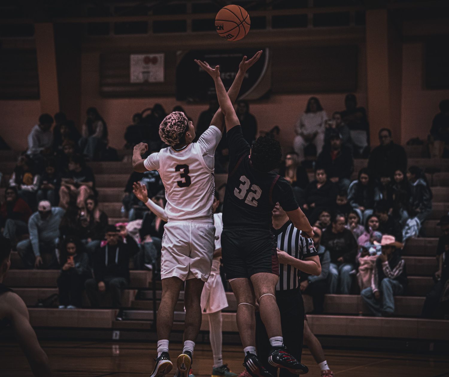 Basketball players competing for the ball during an intense indoor game with spectators in the background.