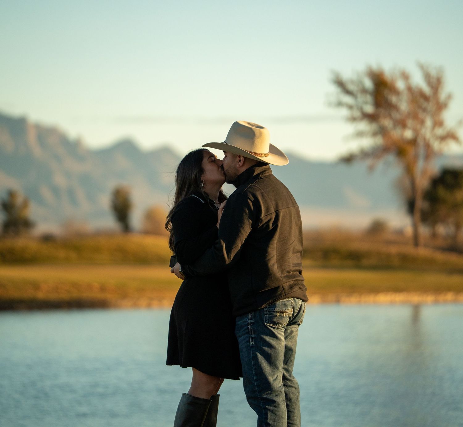 A romantic silhouette of a couple embracing by a lake at sunset with mountains in the background.