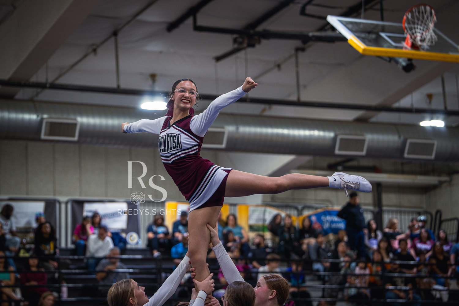 A cheerleader performs a dynamic aerial stunt sequence during an indoor competition event.