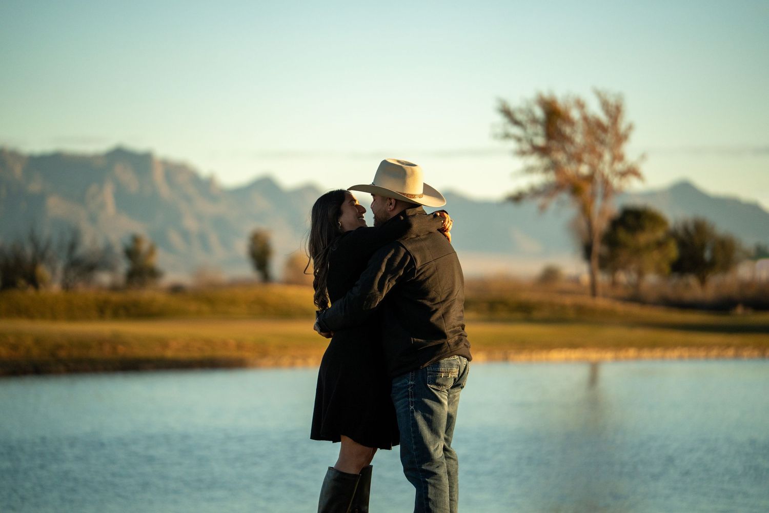 A couple stands together overlooking a scenic mountain lake at sunset with fall foliage in view.