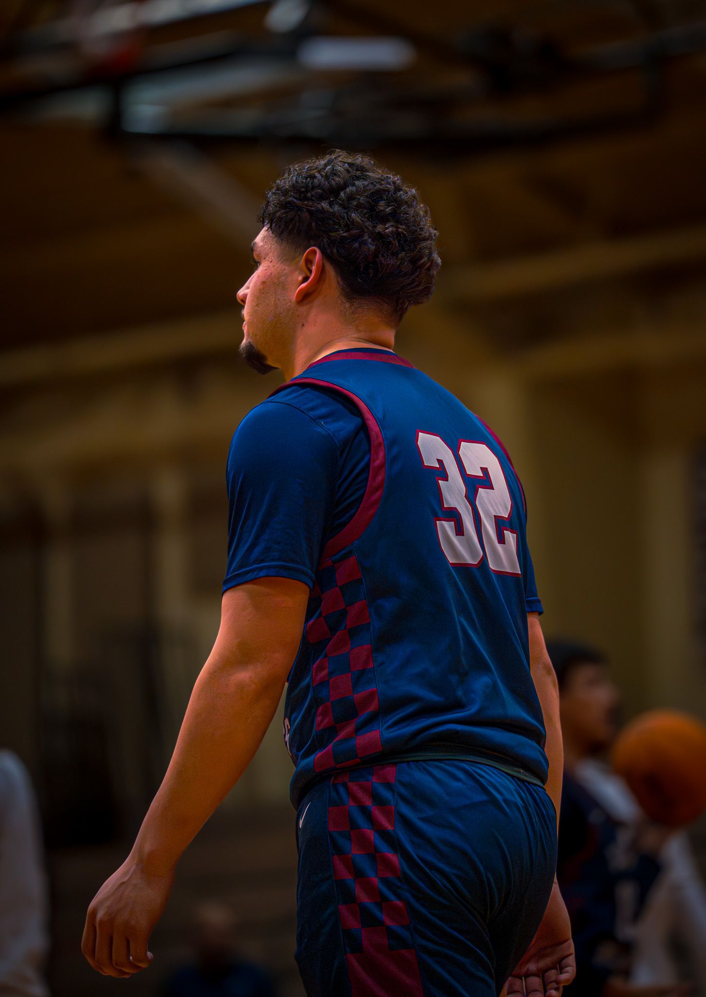 Basketball player wearing navy blue jersey with red stripes moves across court during indoor game.