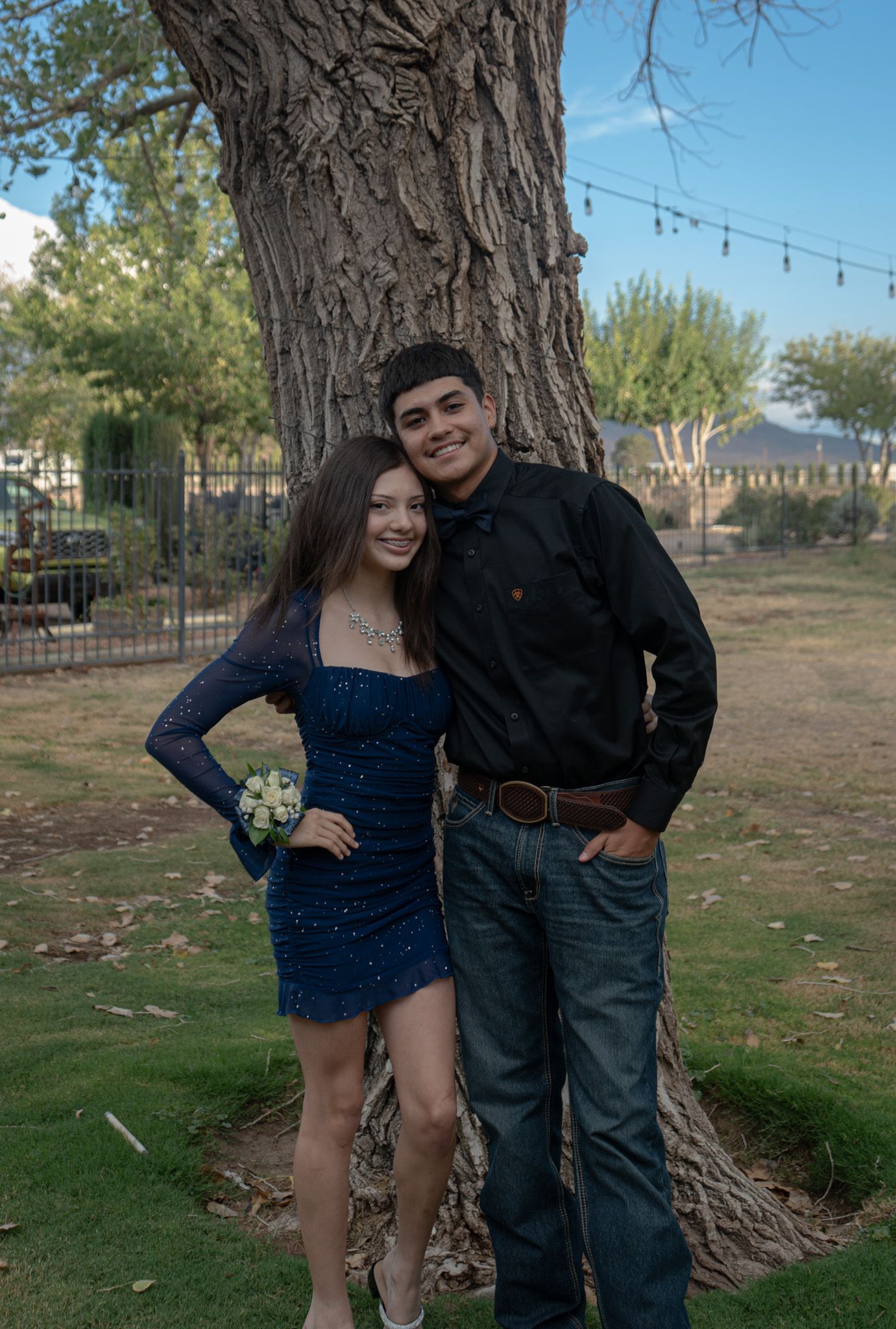 Couple posing together in front of large tree trunk with string lights.