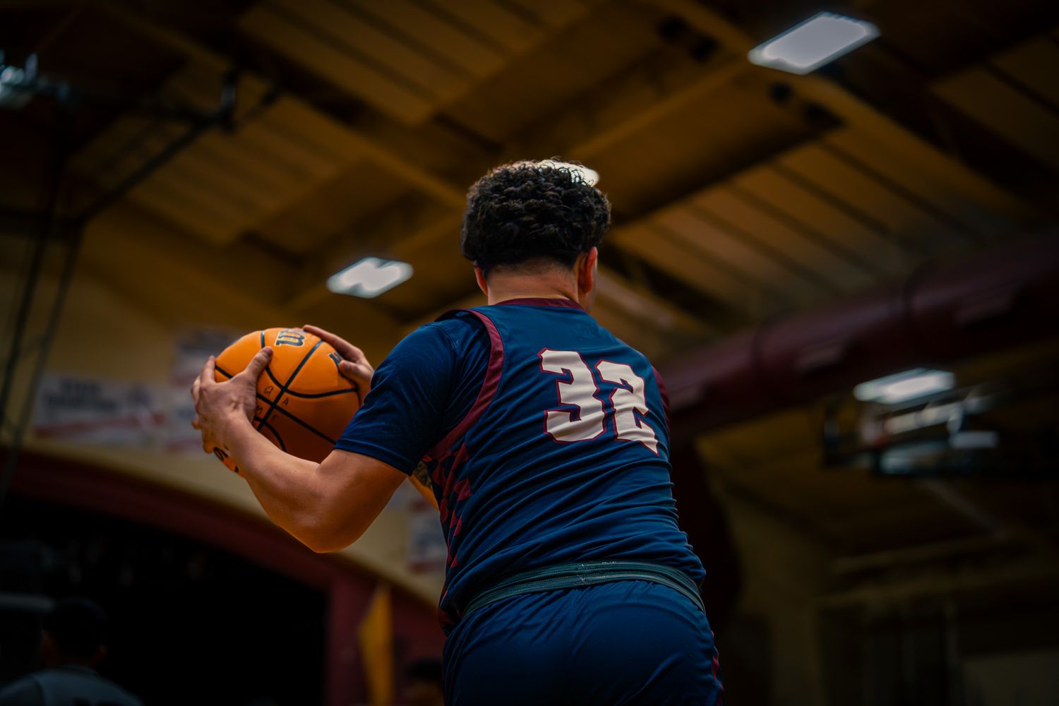 Basketball player wearing jersey number 32 holds ball during indoor game in gymnasium.