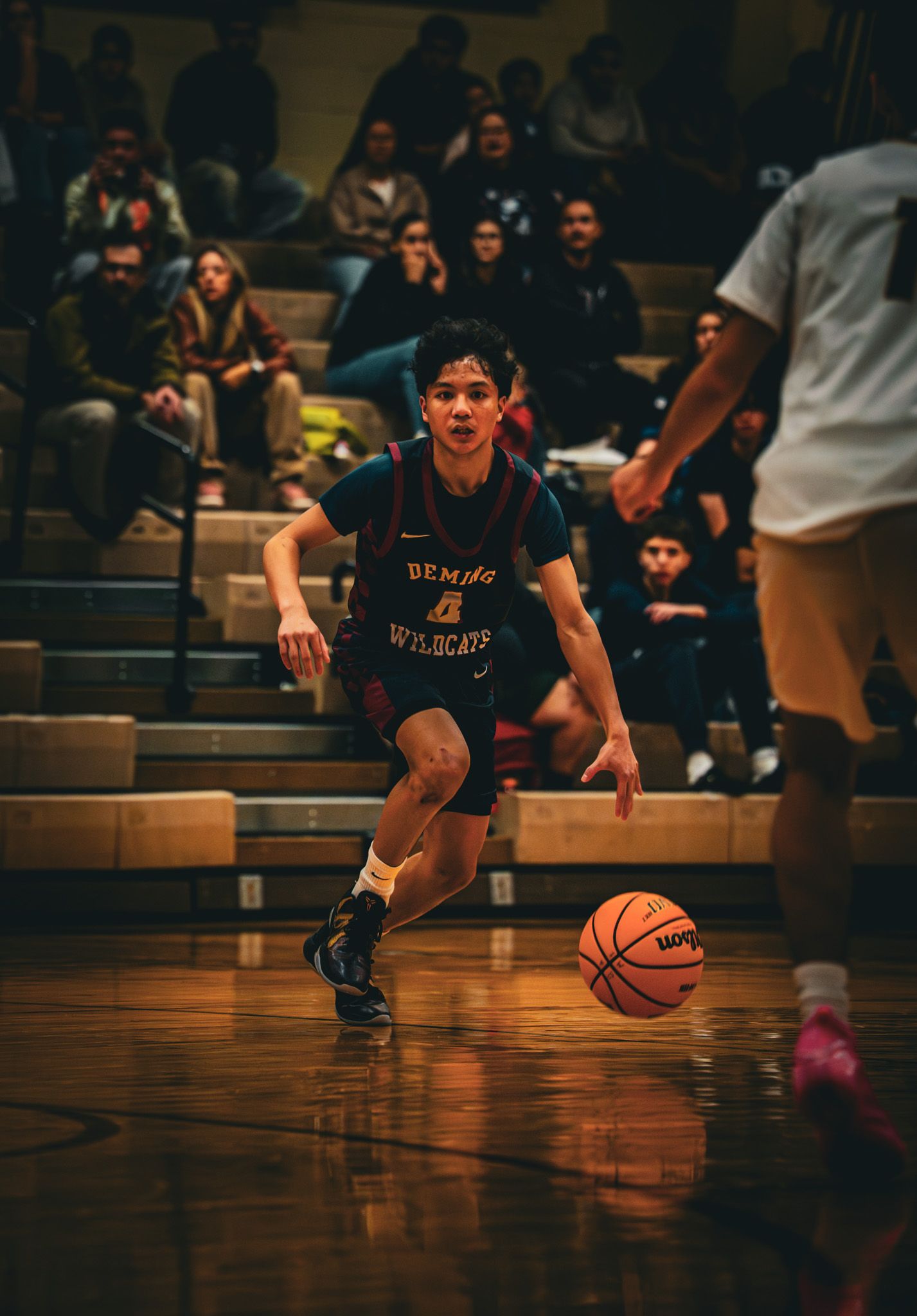 Basketball player in black jersey dribbles low on a shiny wooden court during an indoor game.
