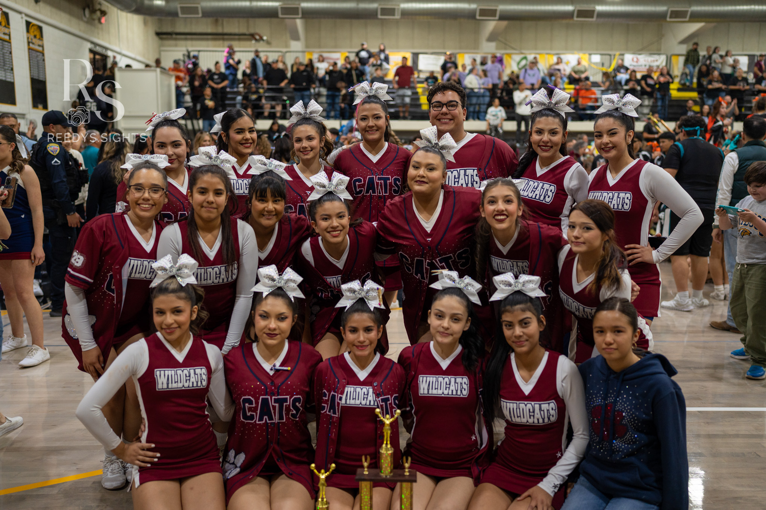A large group of cheerleaders in maroon uniforms pose together for a team photo.