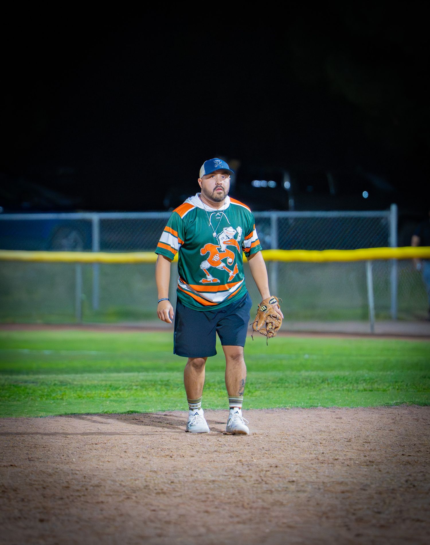 Baseball player crouching in fielding position on dirt infield during evening game.