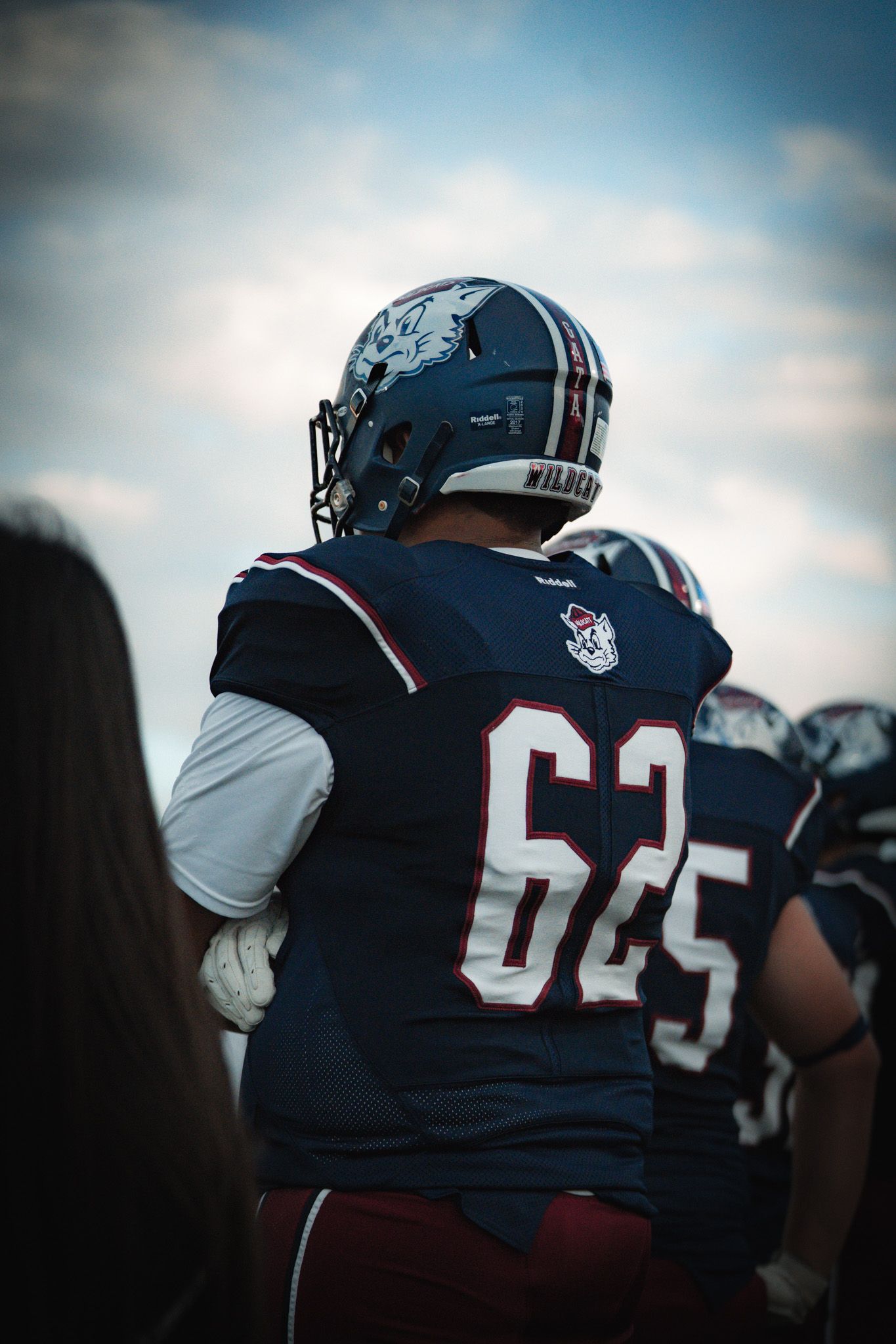 Close-up view of football players in navy blue and white uniforms standing on the sideline during a game.