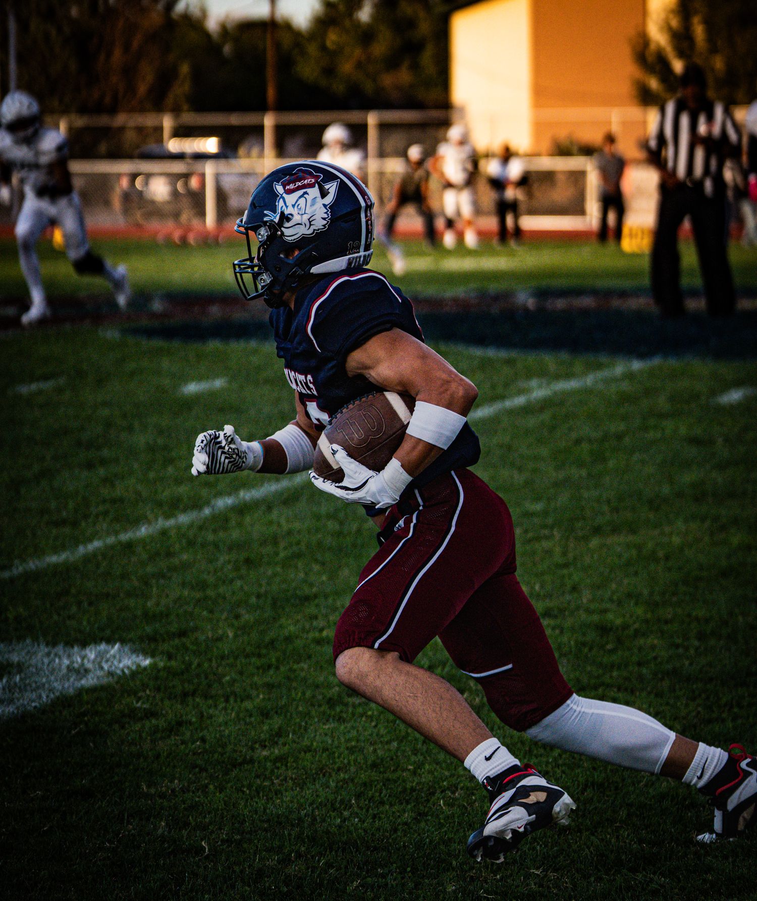 Football player makes a diving catch on the field during sunset.