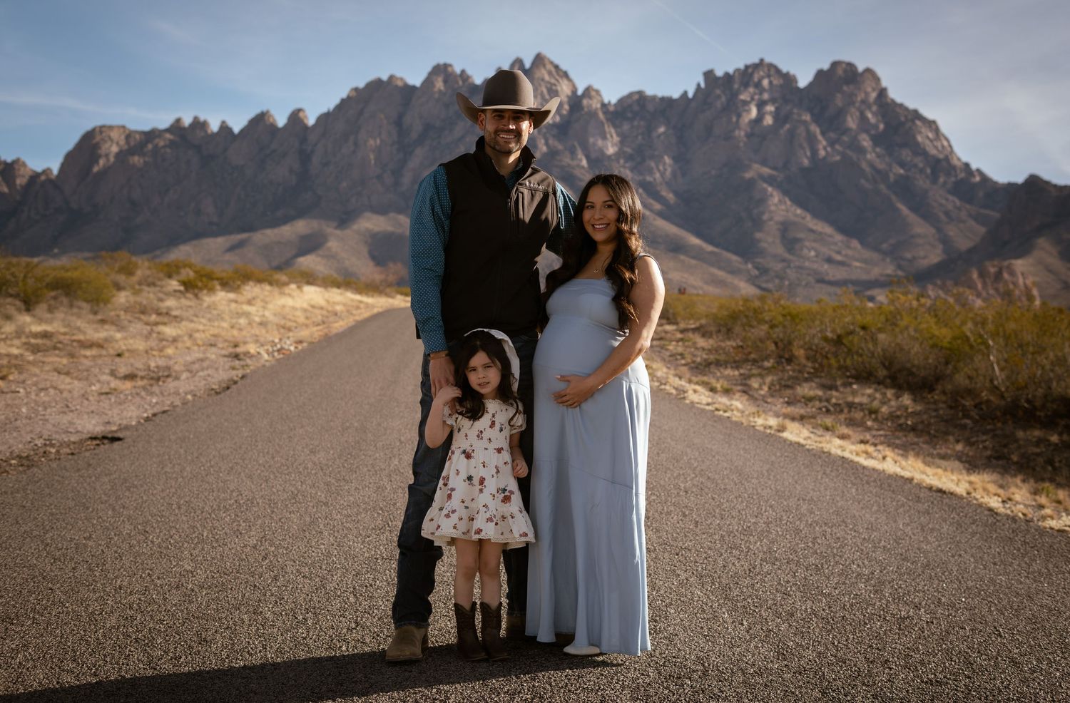 A family stands together on an empty desert road with the dramatic Organ Mountains rising in the background near Las Cruces.