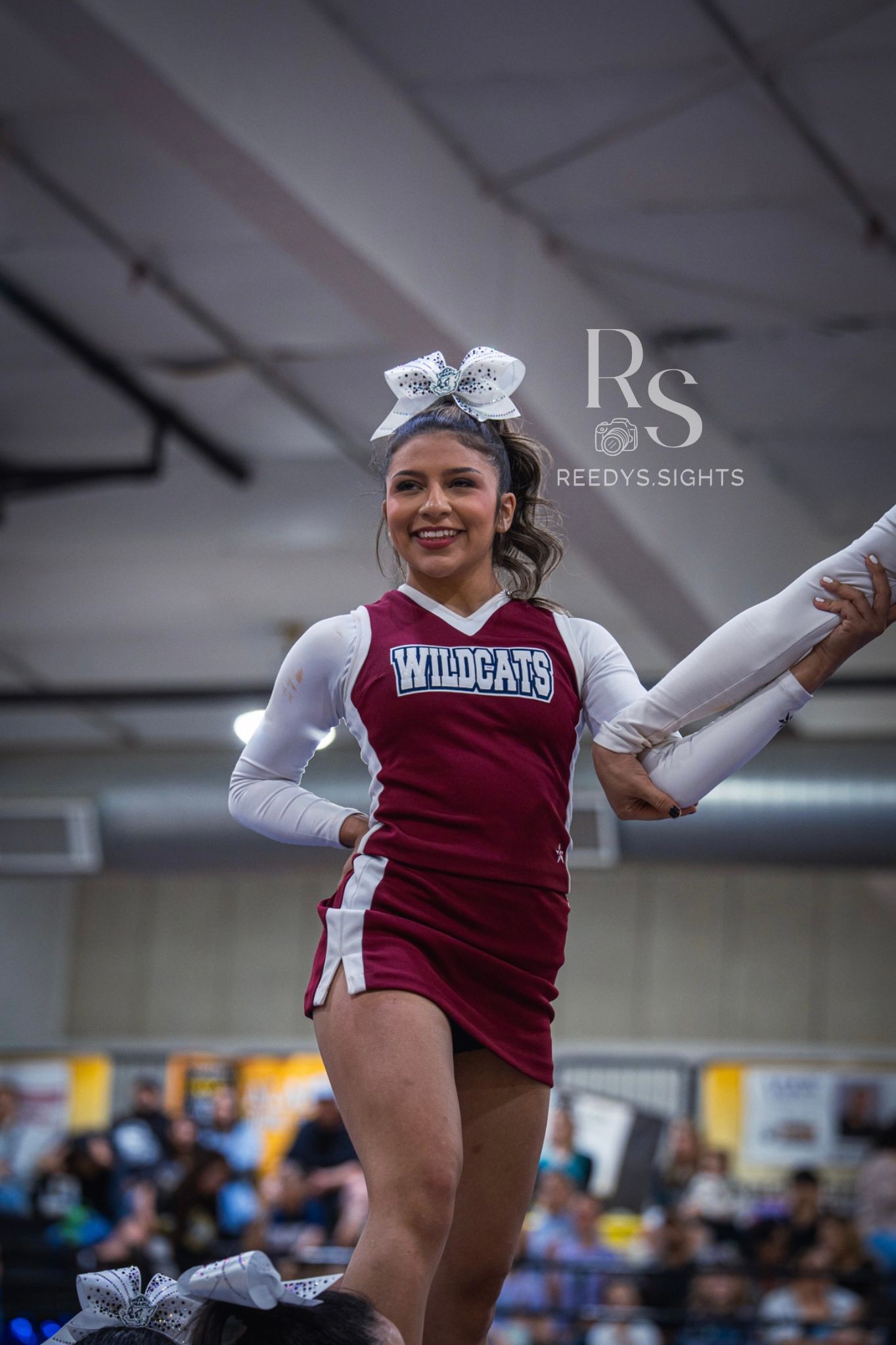 Cheerleaders performing synchronized dance moves in burgundy and white uniforms at an indoor competition.
