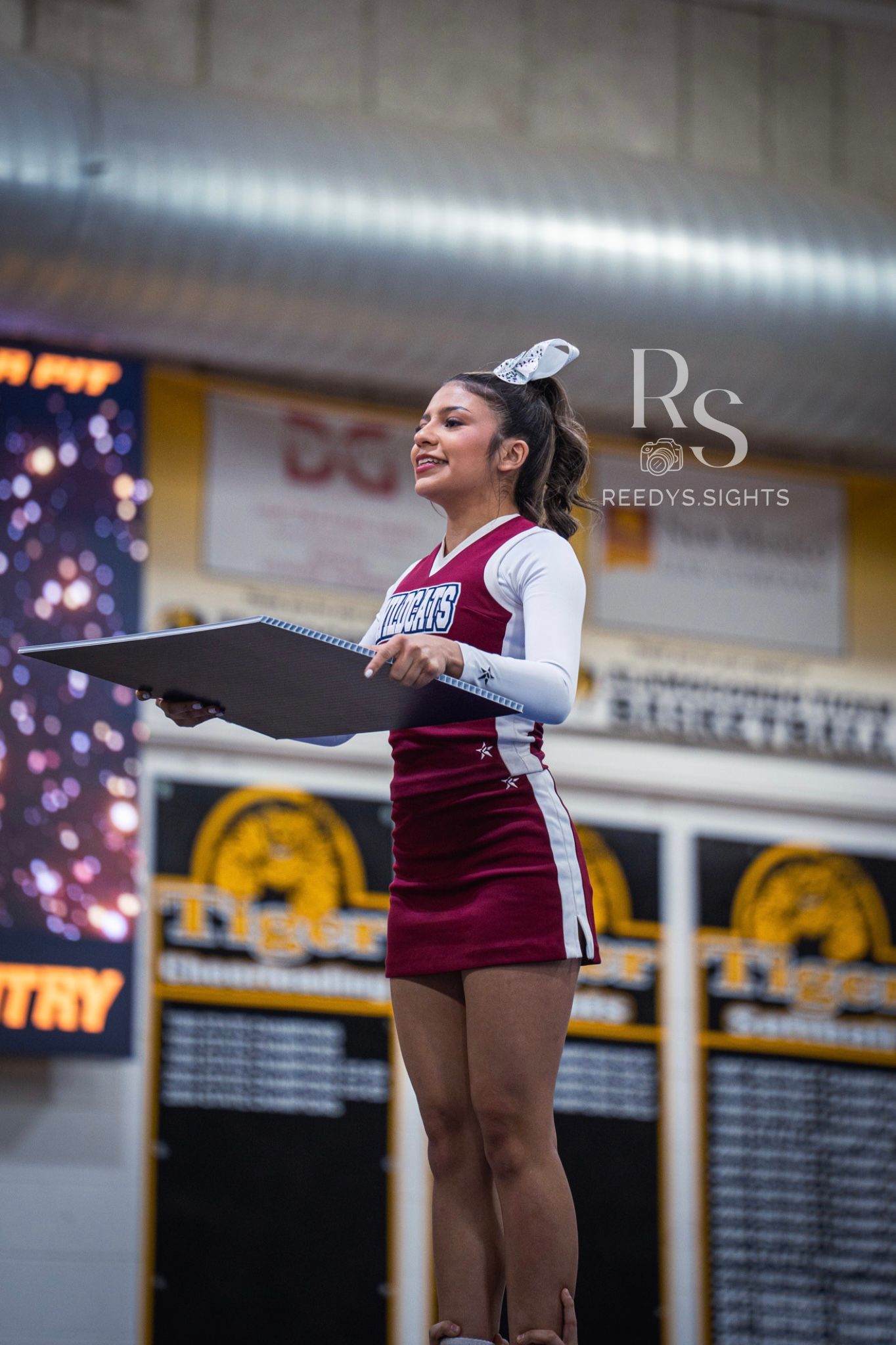 Cheerleader in maroon uniform performs a dance routine at an indoor competition venue.