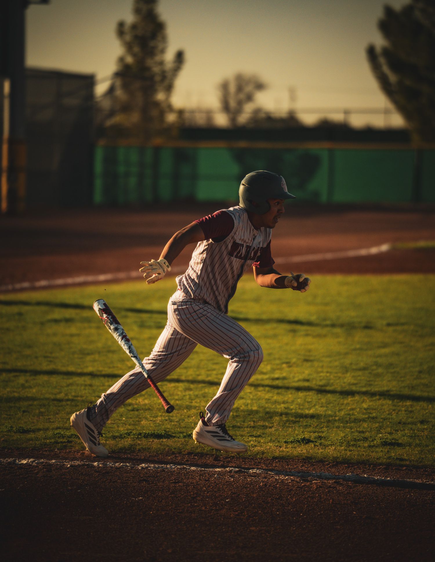 Baseball player sprinting from home plate during golden hour on baseball field.
