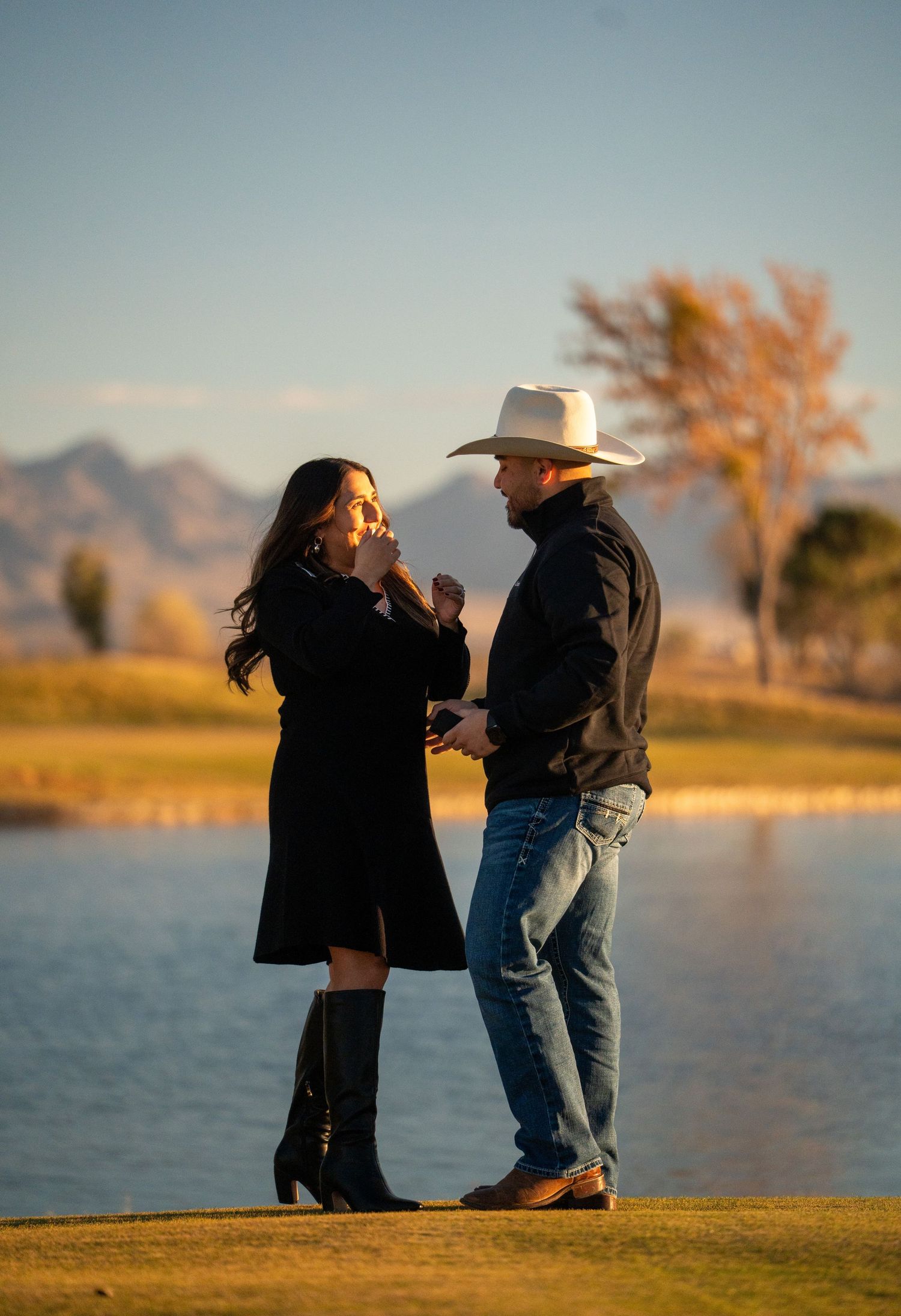 Silhouetted figures share a tender moment by a lake with mountains and autumn trees in background.