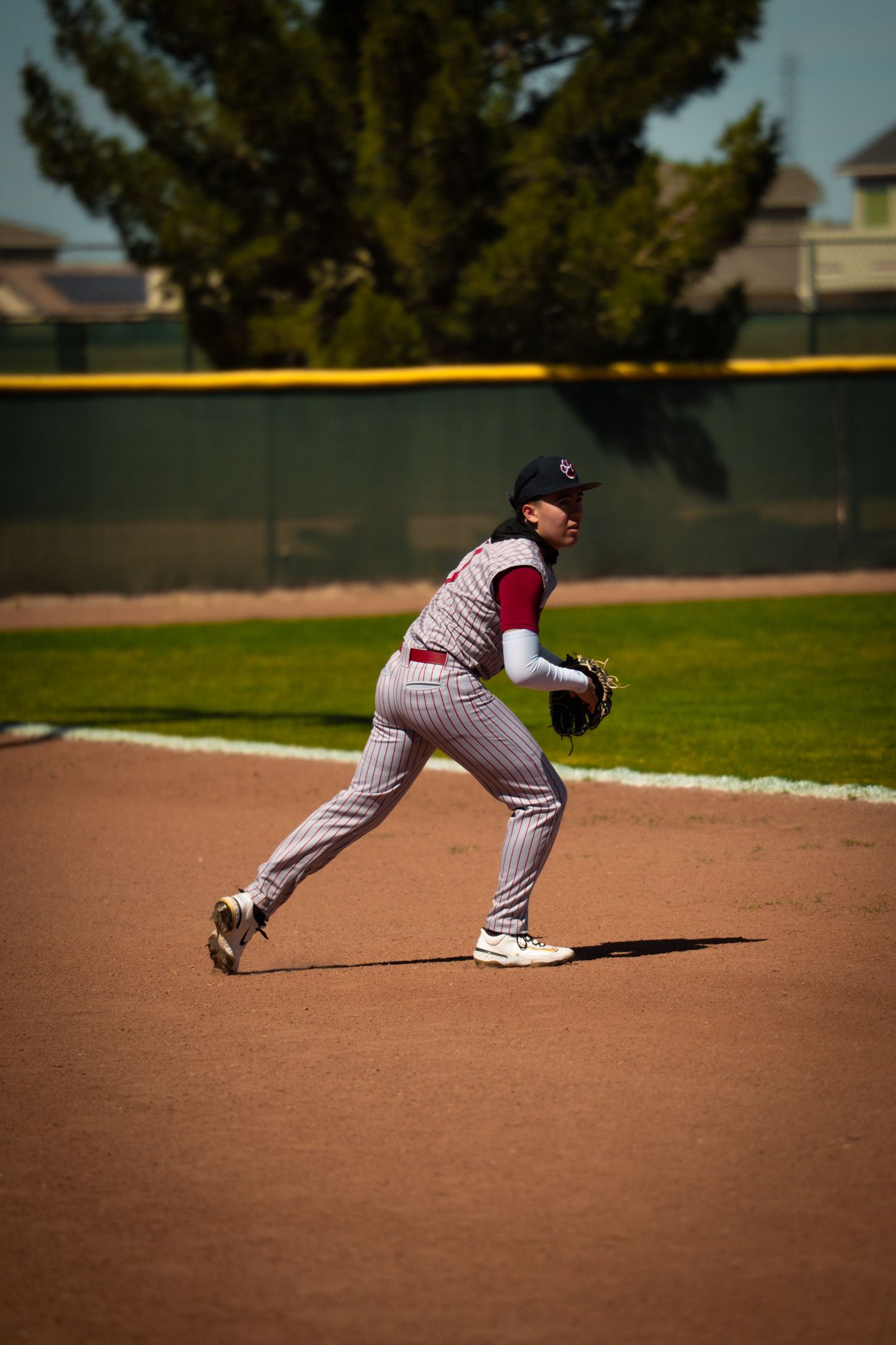 Baseball player in pinstripes demonstrates fielding technique sequence on dirt infield during practice.