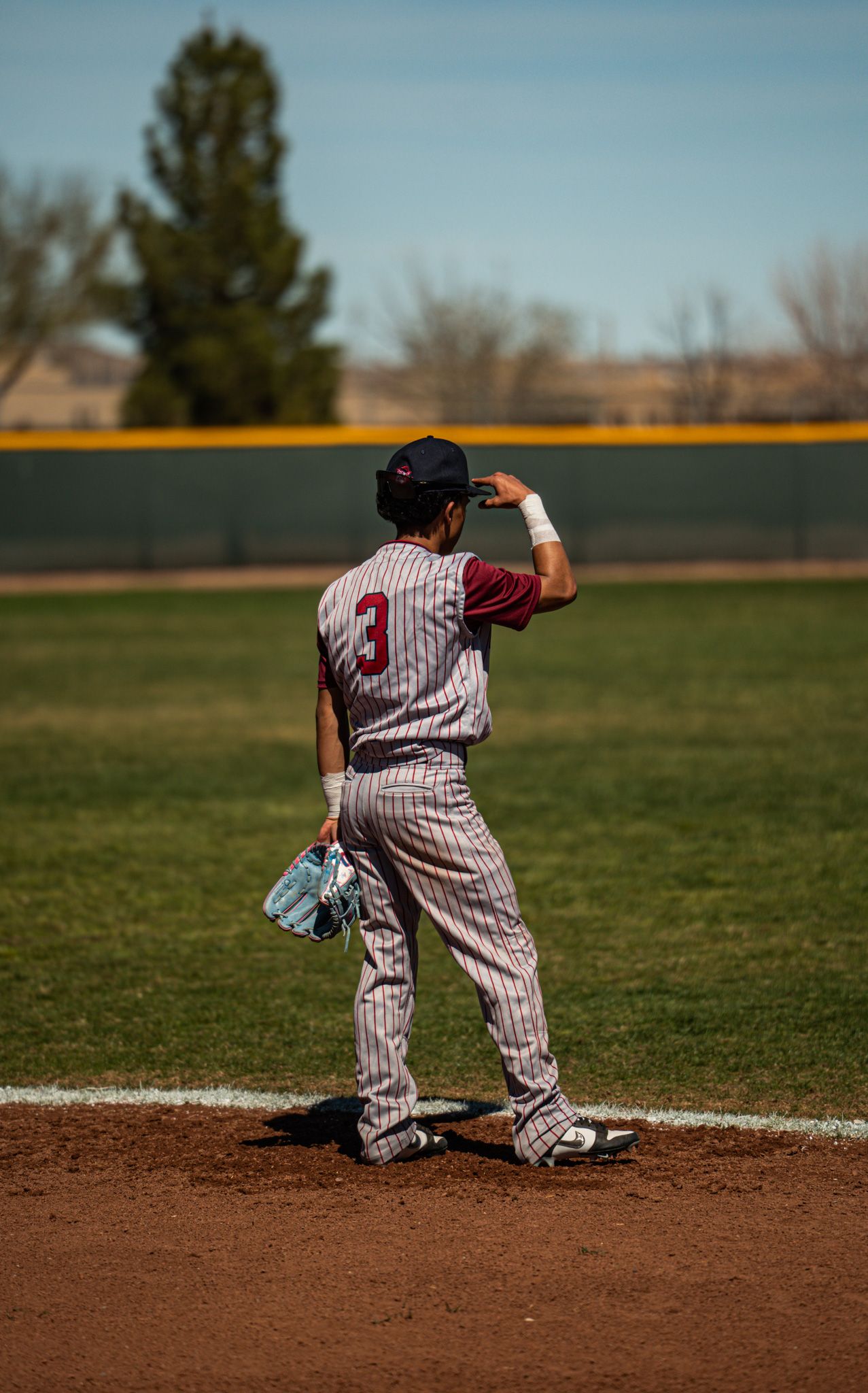 Baseball player in pinstriped uniform stands on pitcher's mound during sunny day game at outdoor baseball field.