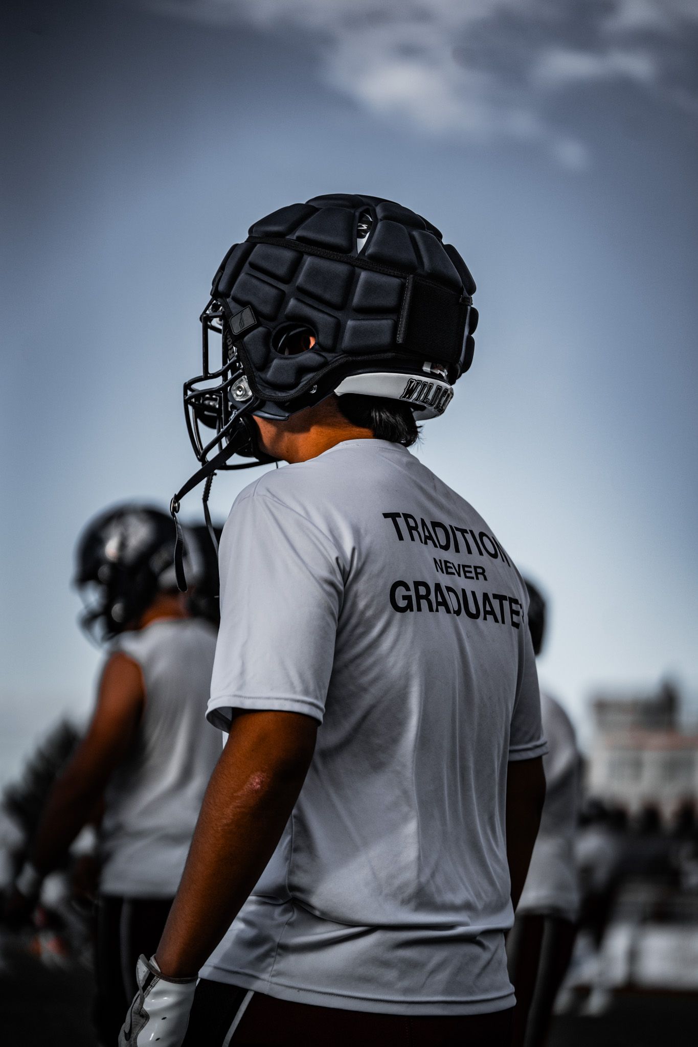 Football player wearing black protective helmet and white t-shirt with 'Trust the Graduate' text during practice session.