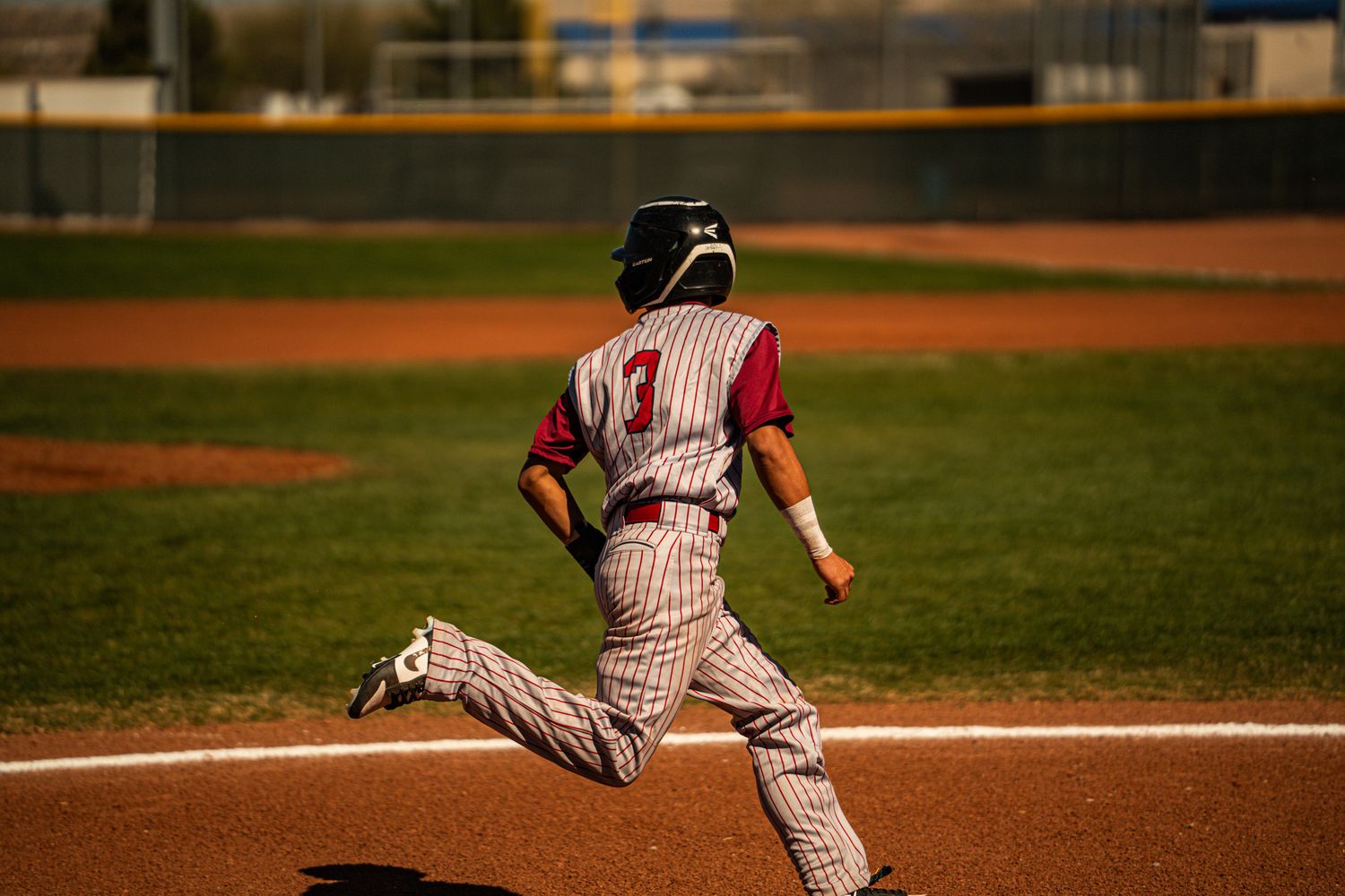 Baseball player slides into home plate during a game on a dirt infield at sunset.