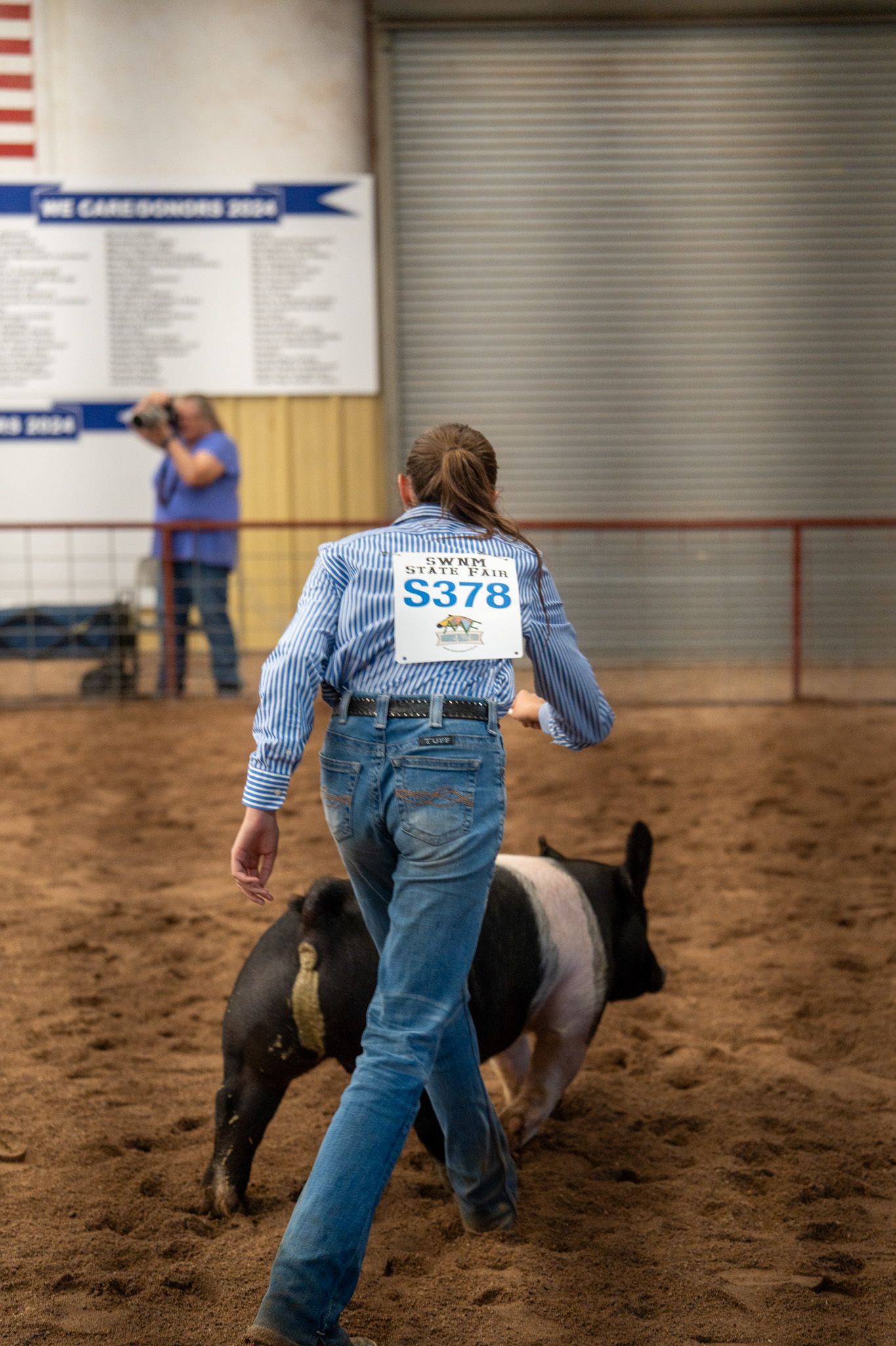 Contestant in blue striped shirt and jeans competes in calf roping event at indoor rodeo arena.