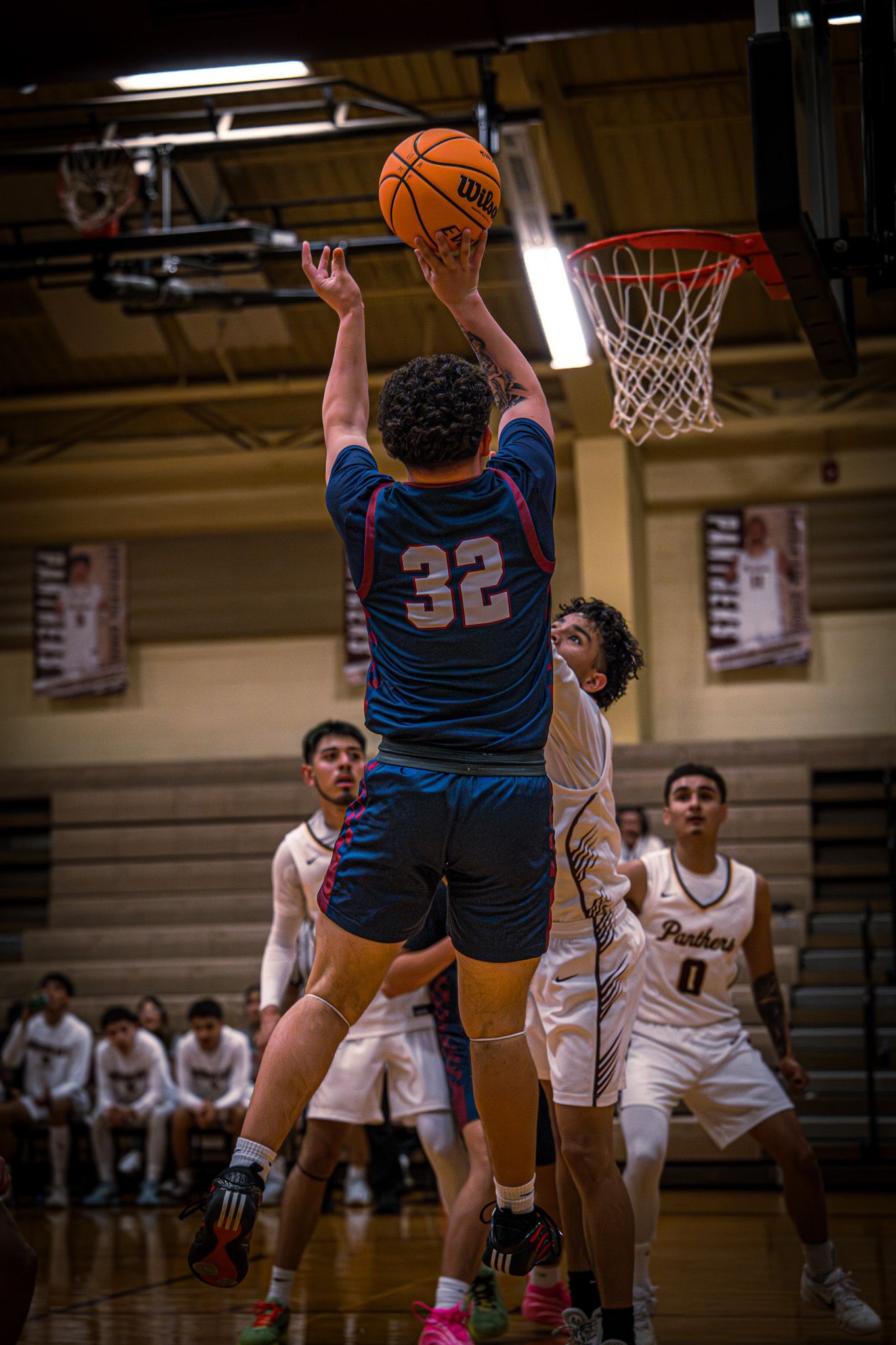 Basketball player in blue jersey number 32 goes up for a layup during an intense game against players in white uniforms.