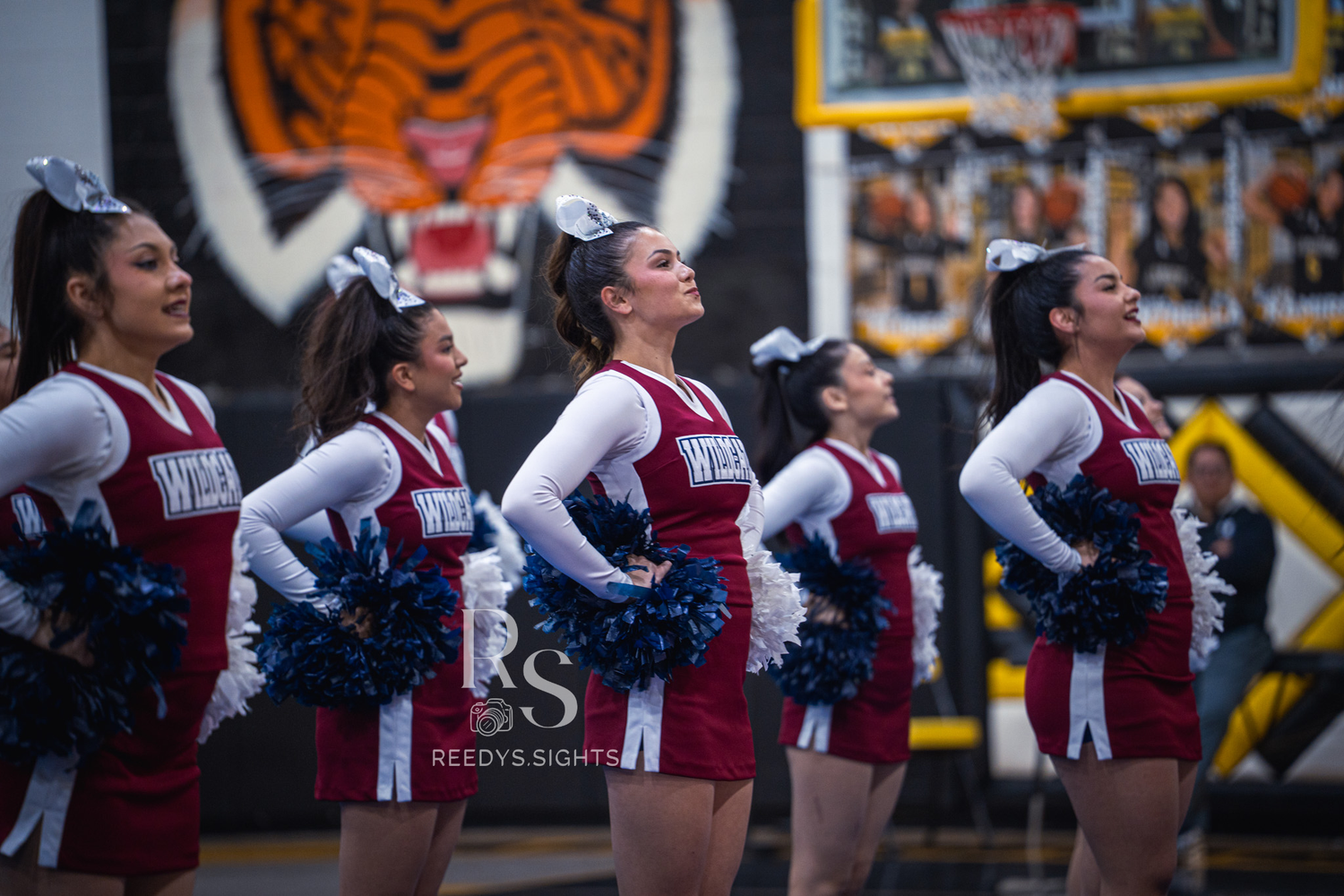 High school cheerleaders perform synchronized dance routine during sports event in maroon and white uniforms.