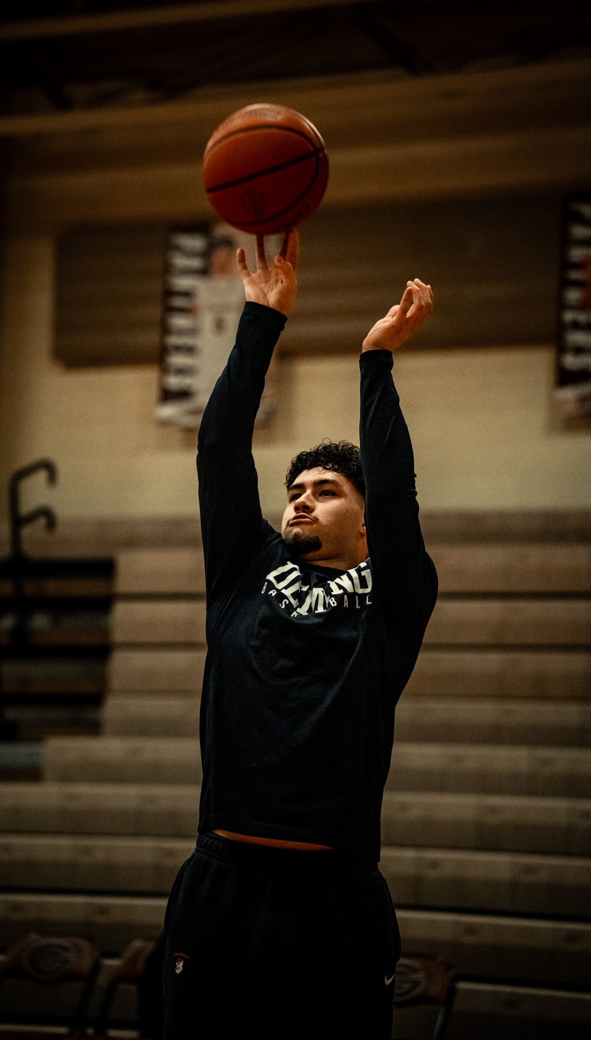 Basketball player in black practices shooting form in an empty gymnasium.