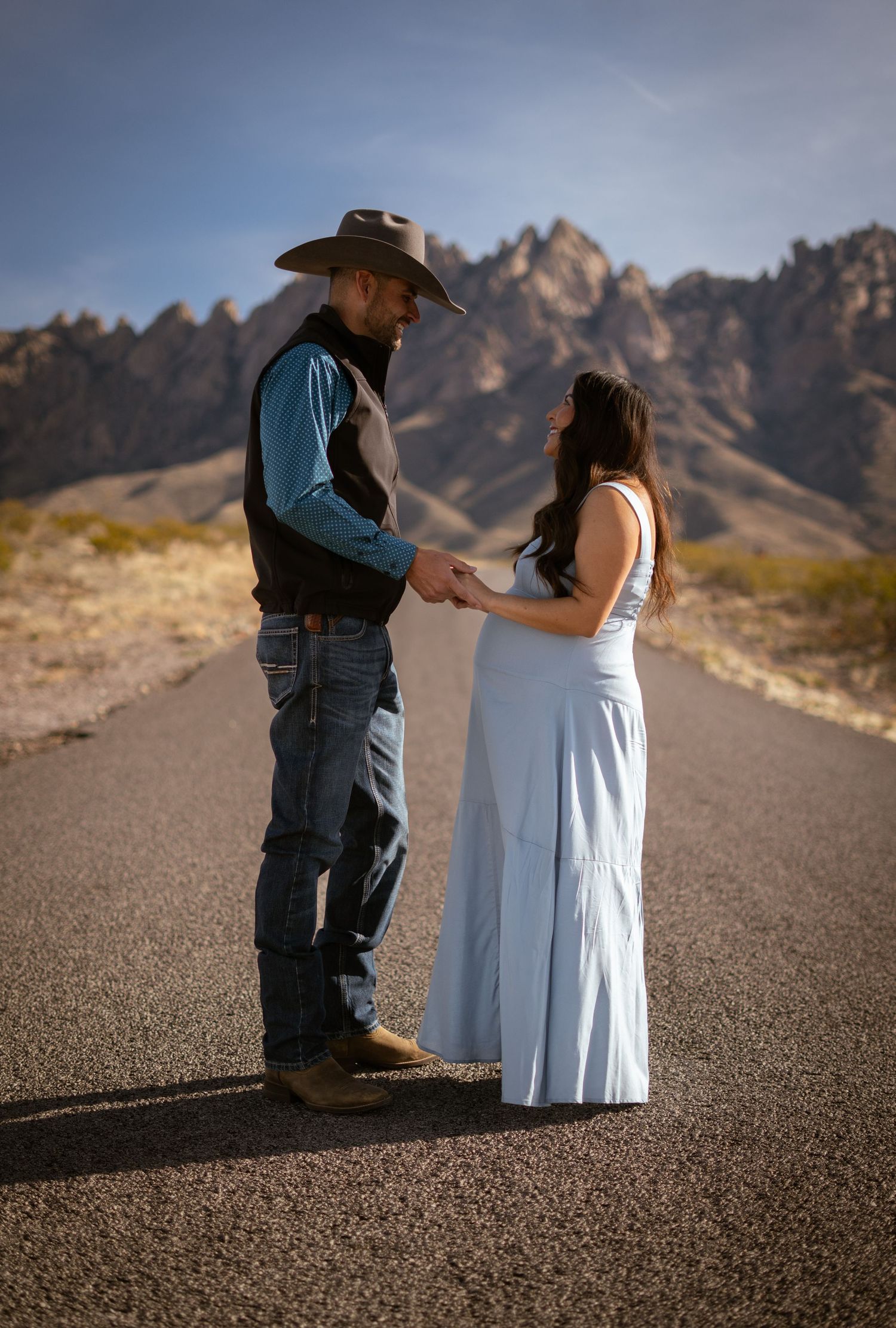 A couple stands together on a desert road with rugged mountains in the background near Las Cruces, New Mexico.