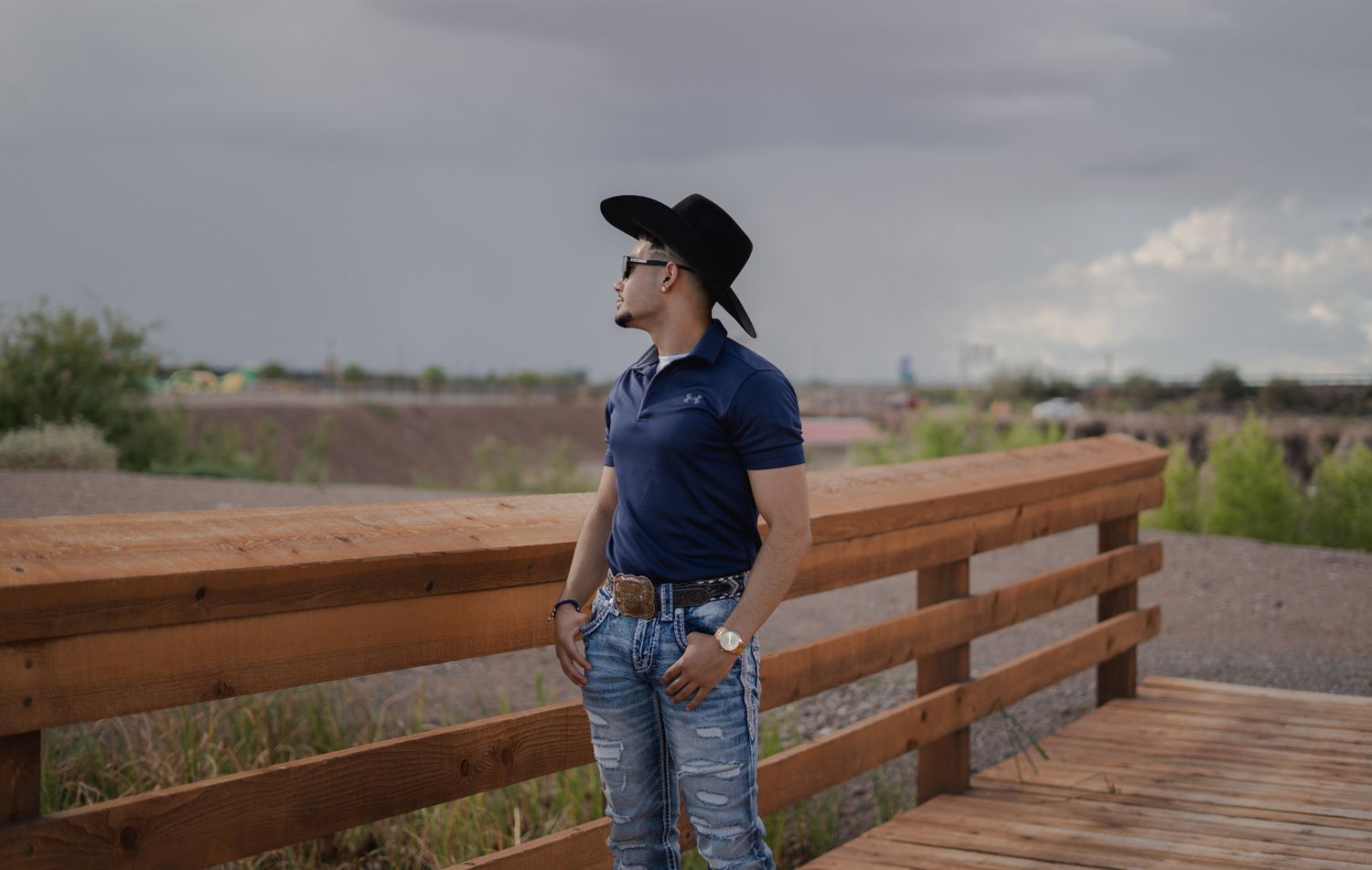 Person in western attire standing on wooden deck overlooking rural landscape.