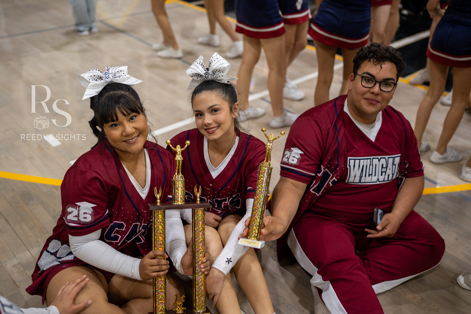 High school cheerleaders in maroon and navy uniforms gather together during a sports event.