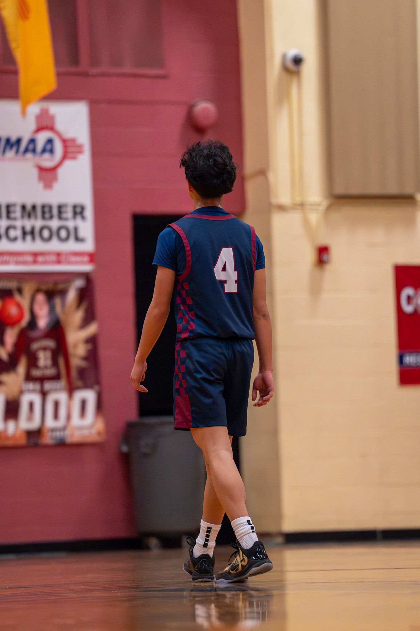 Basketball player wearing jersey number 4 runs across the gymnasium court during a game.