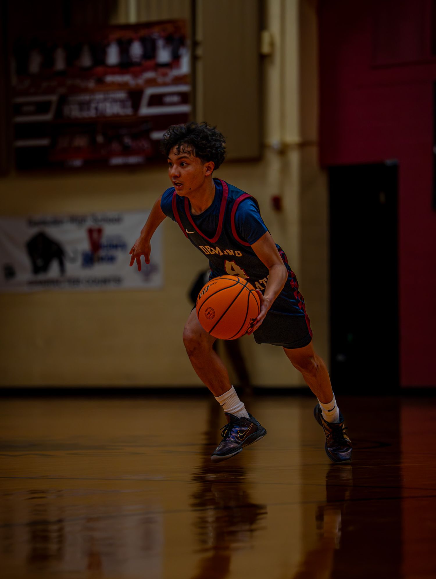 Young basketball player dribbles low in defensive stance on shiny gymnasium floor.