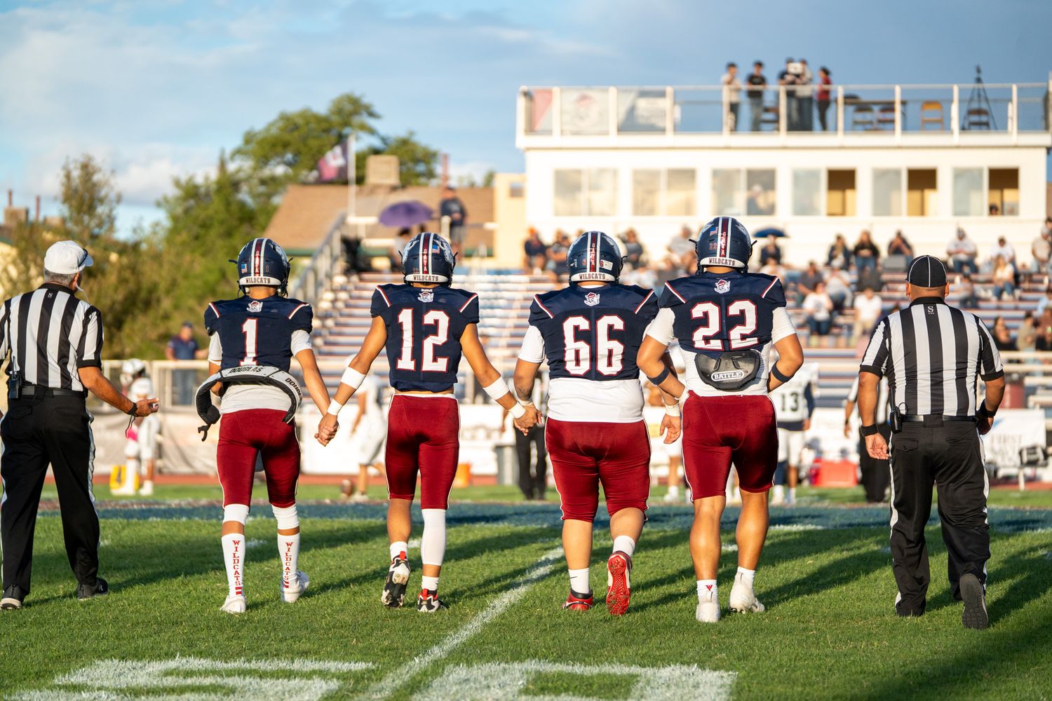 Football players and referees walk on the field during a game with jersey numbers 12, 66 and 22 visible.
