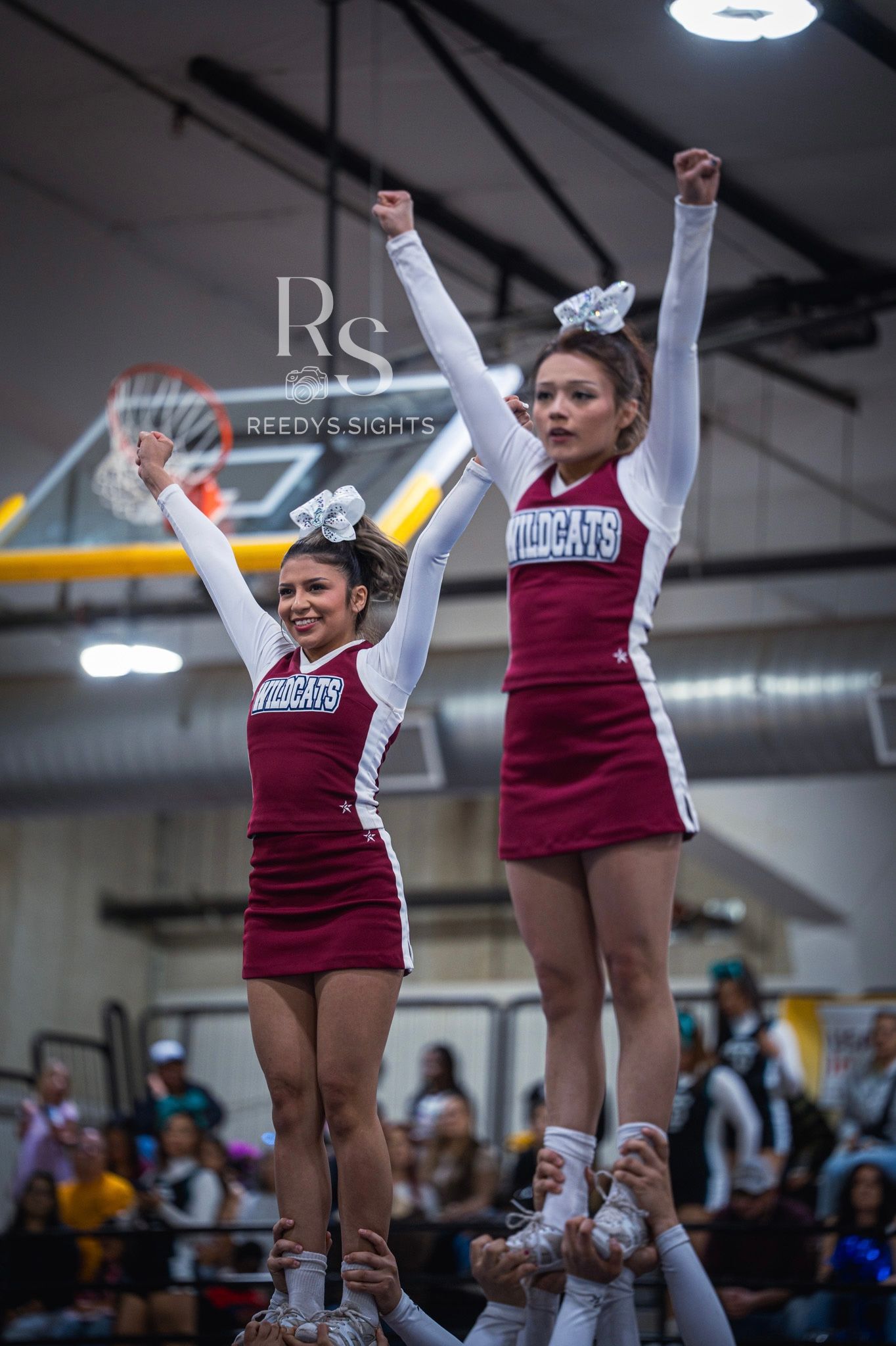 Cheerleaders in maroon and white uniforms perform a stunt lift during an indoor competition.