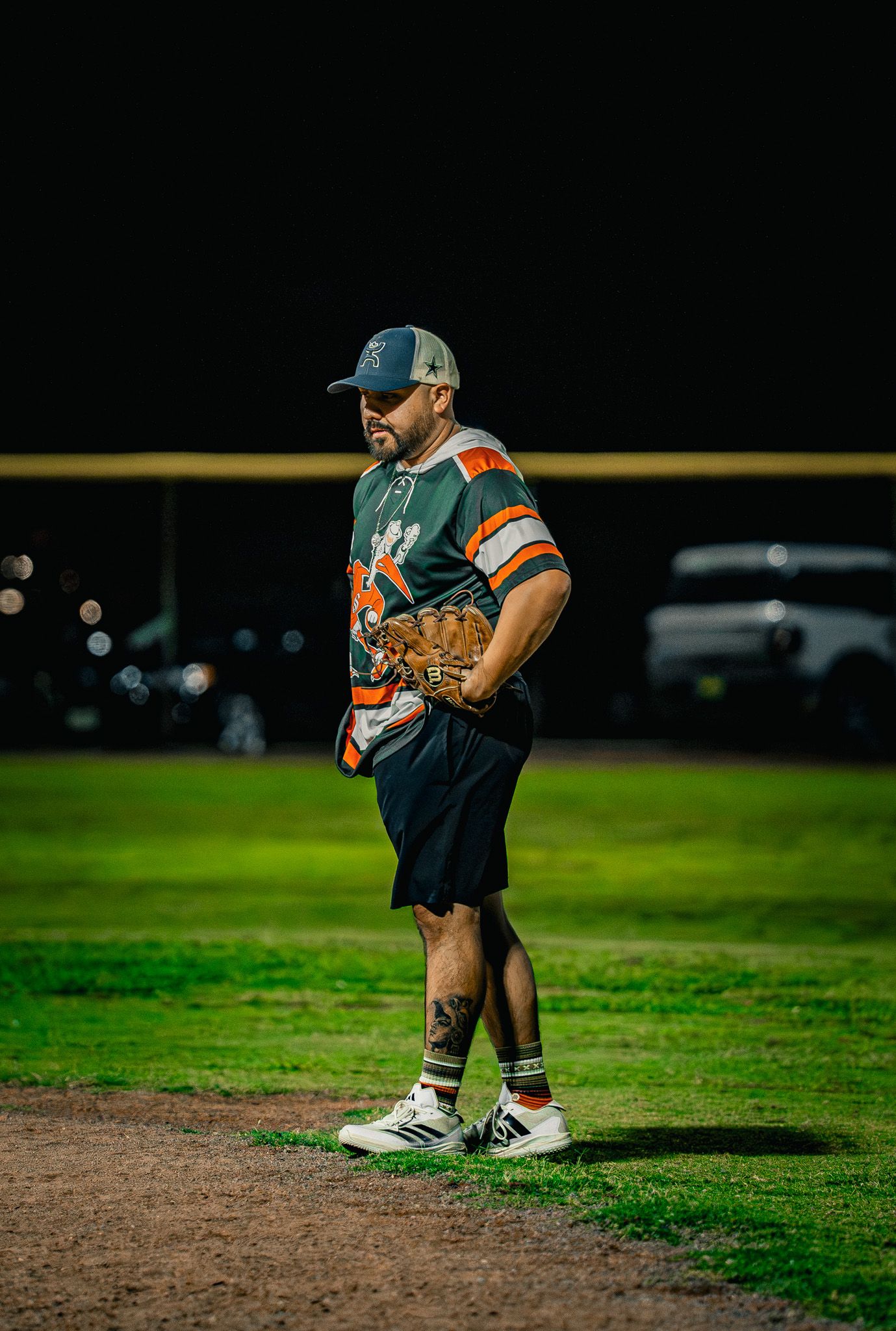 Baseball player in orange and black uniform crouches on infield dirt during daytime game.
