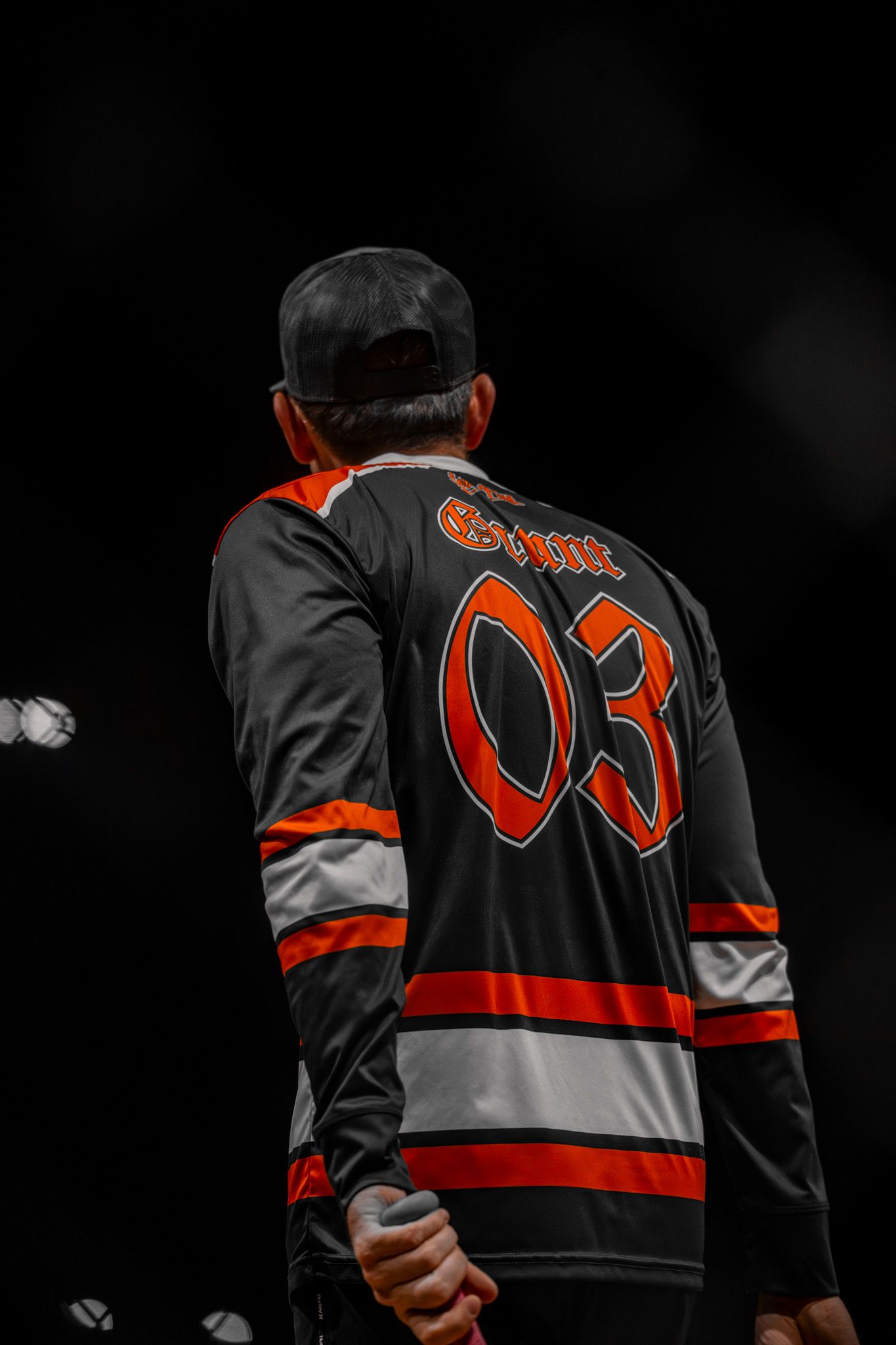 Hockey player wearing black and orange jersey number 03 viewed from behind.