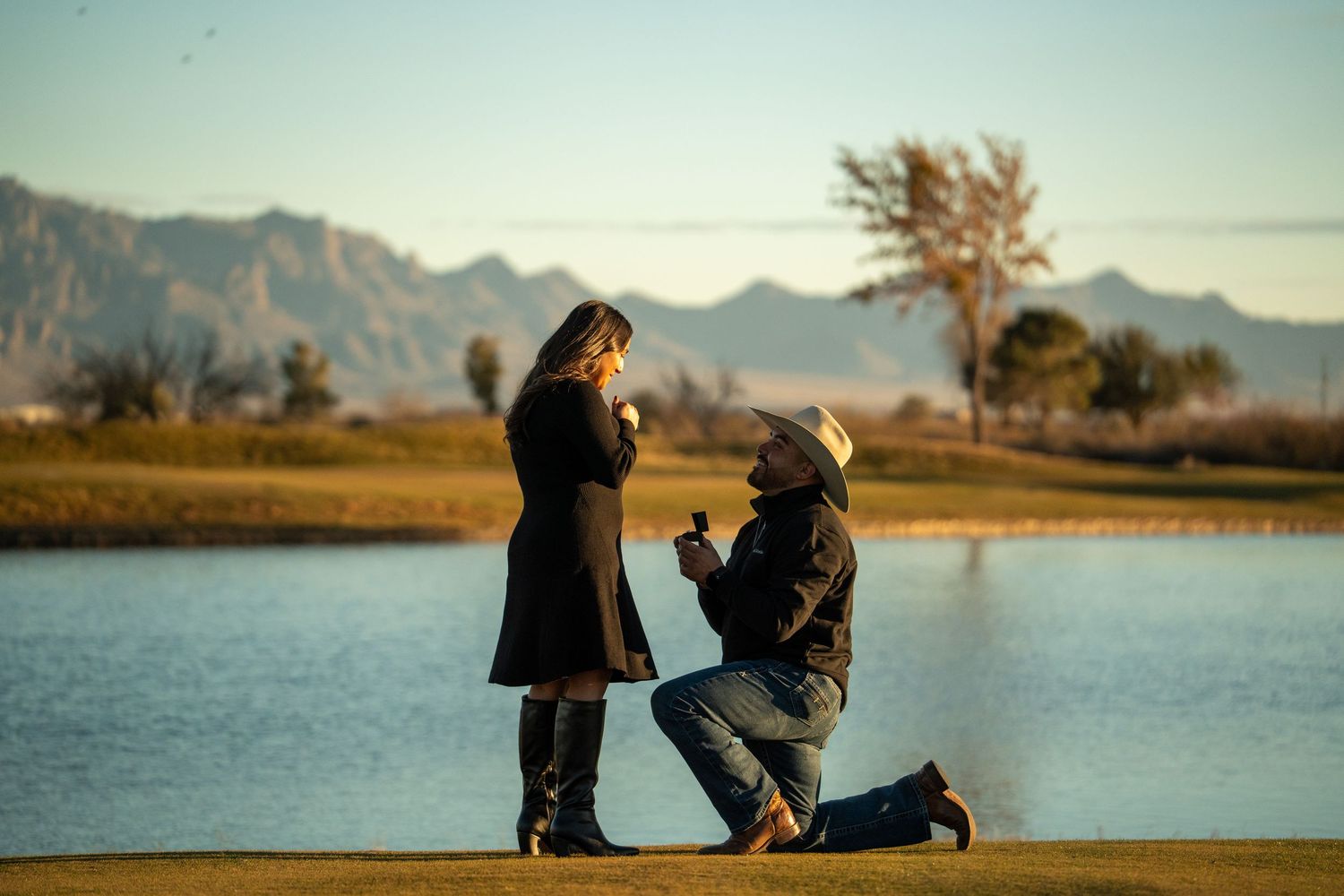 Silhouetted figures share tender moments along a lake shore at sunset with mountains in the background.