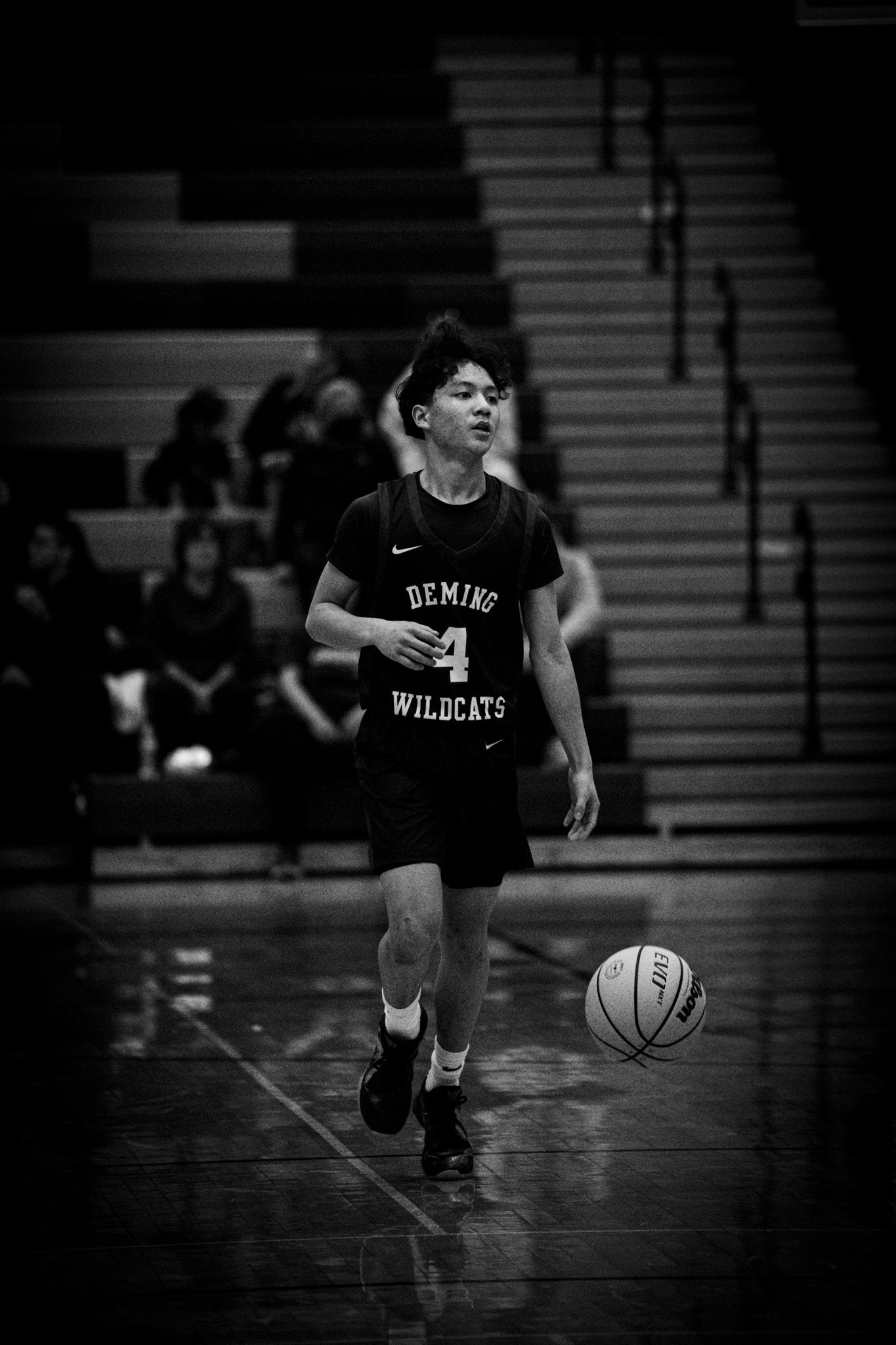 Youth basketball player in Wildcats jersey dribbles ball during game on indoor court.