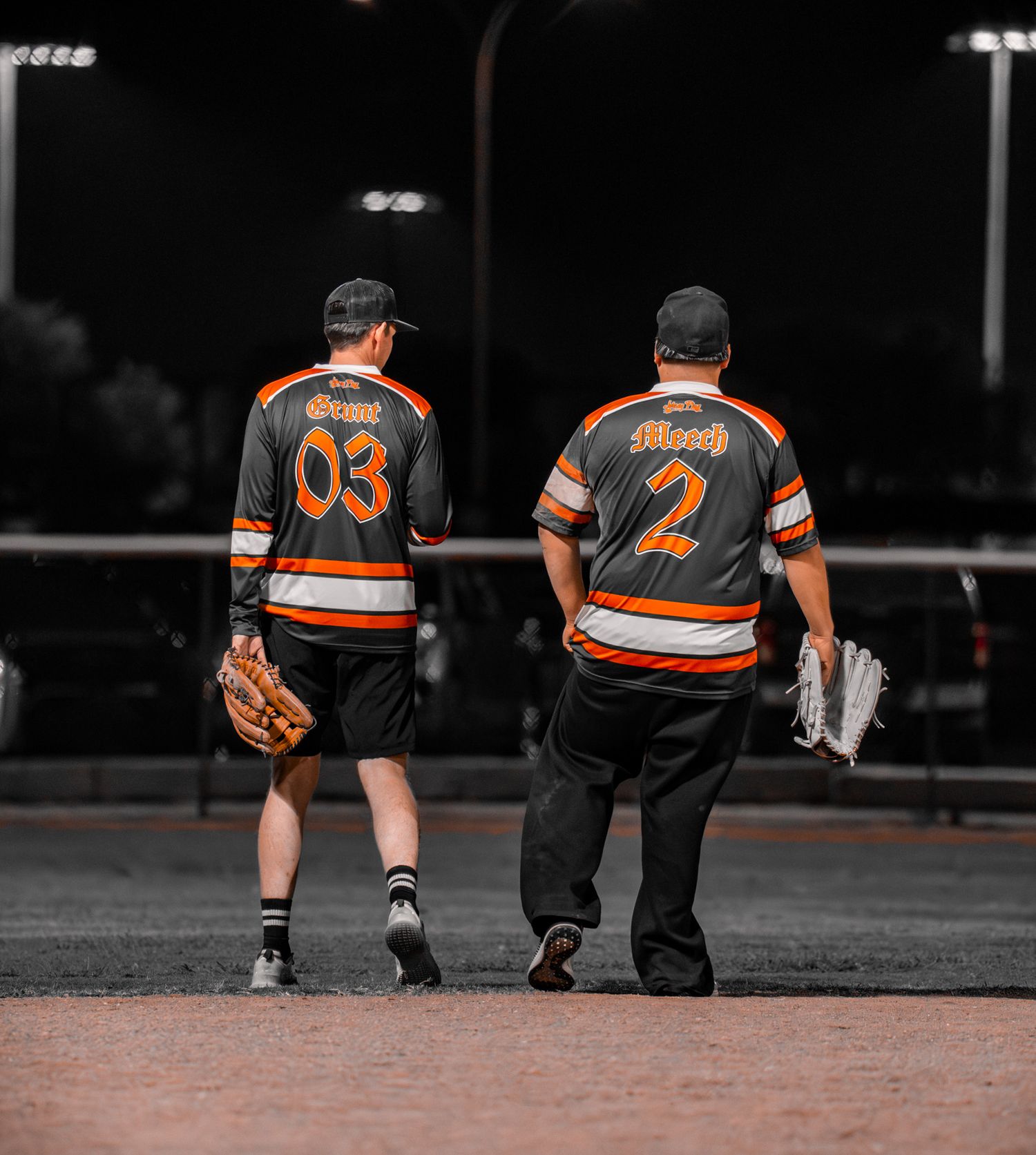 Baseball players in orange and black uniforms kneel on field during game in selective color photography.