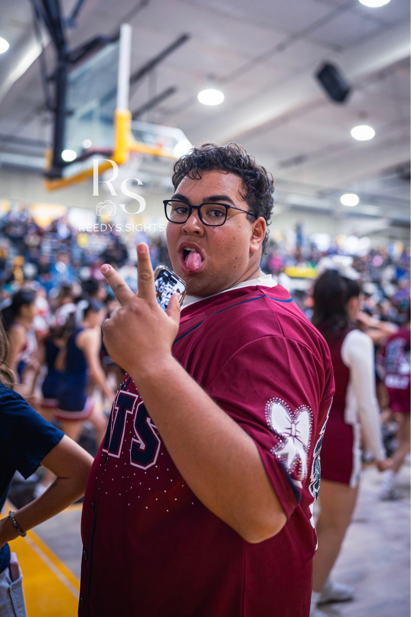 An enthusiastic fan in a maroon jersey cheers excitedly at an indoor sporting event.