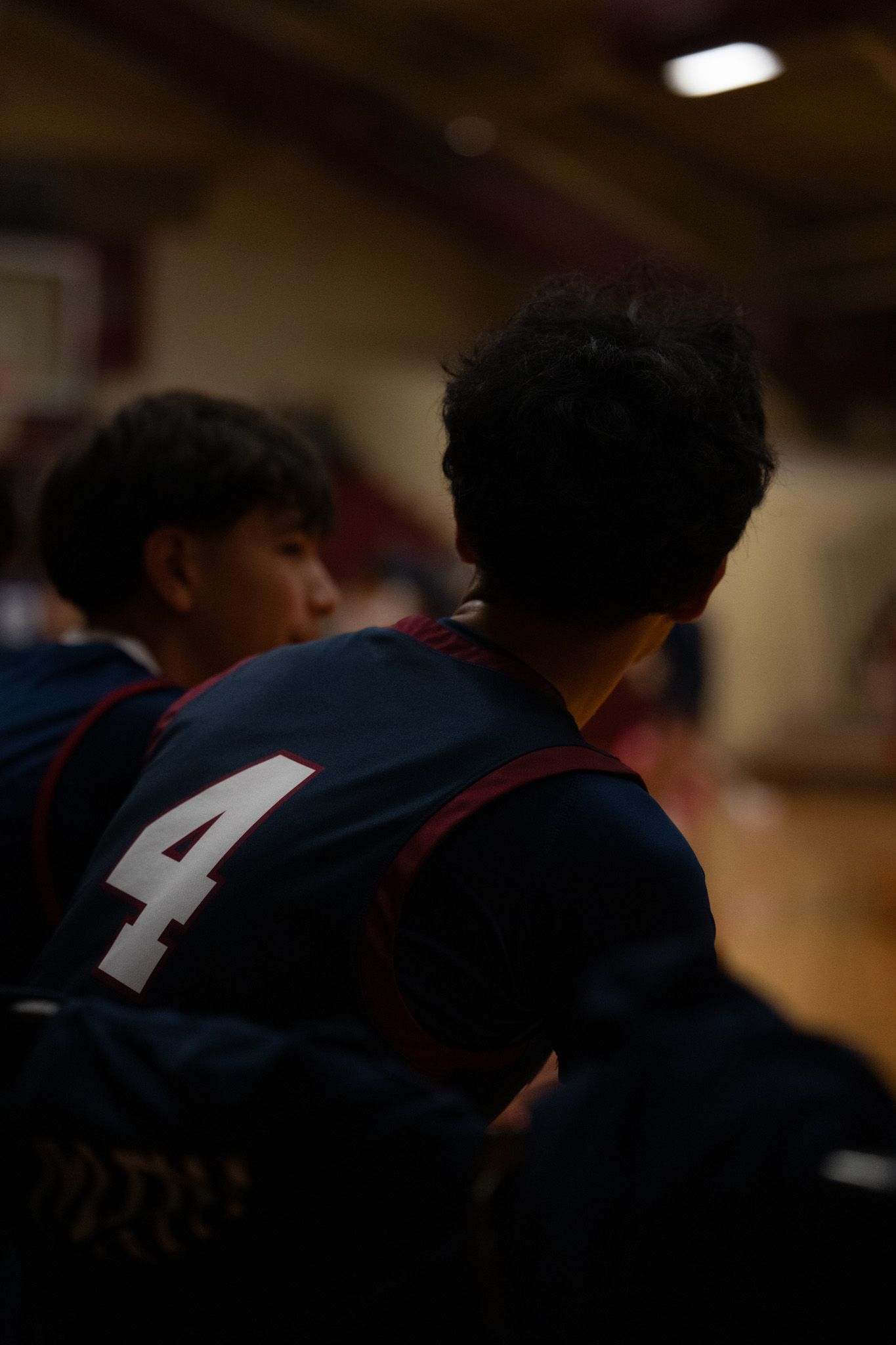 Basketball player wearing jersey number 4 in dark uniform shown from behind during indoor game.