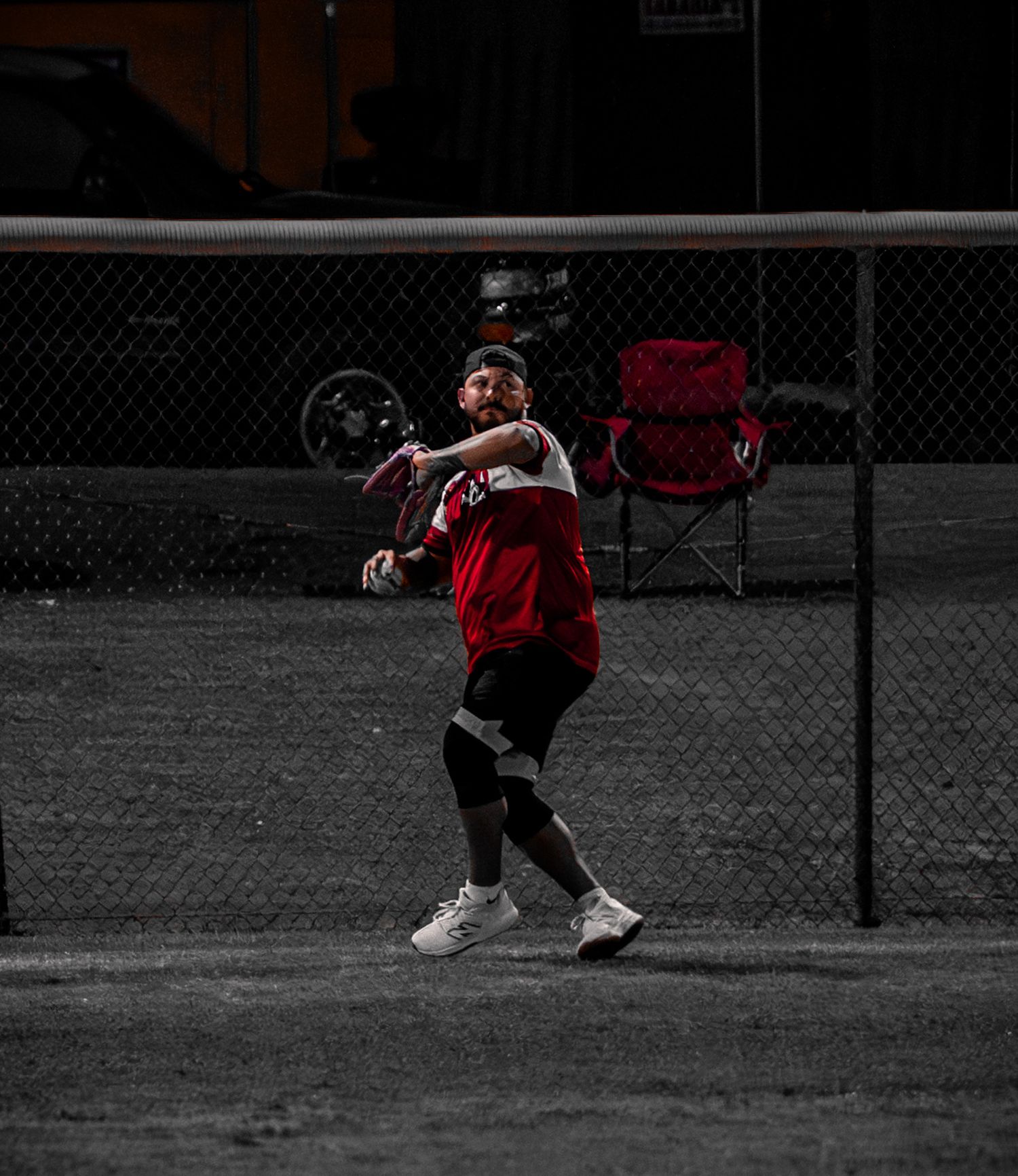 A baseball player in a black and red uniform winds up to throw a pitch on a desaturated field.