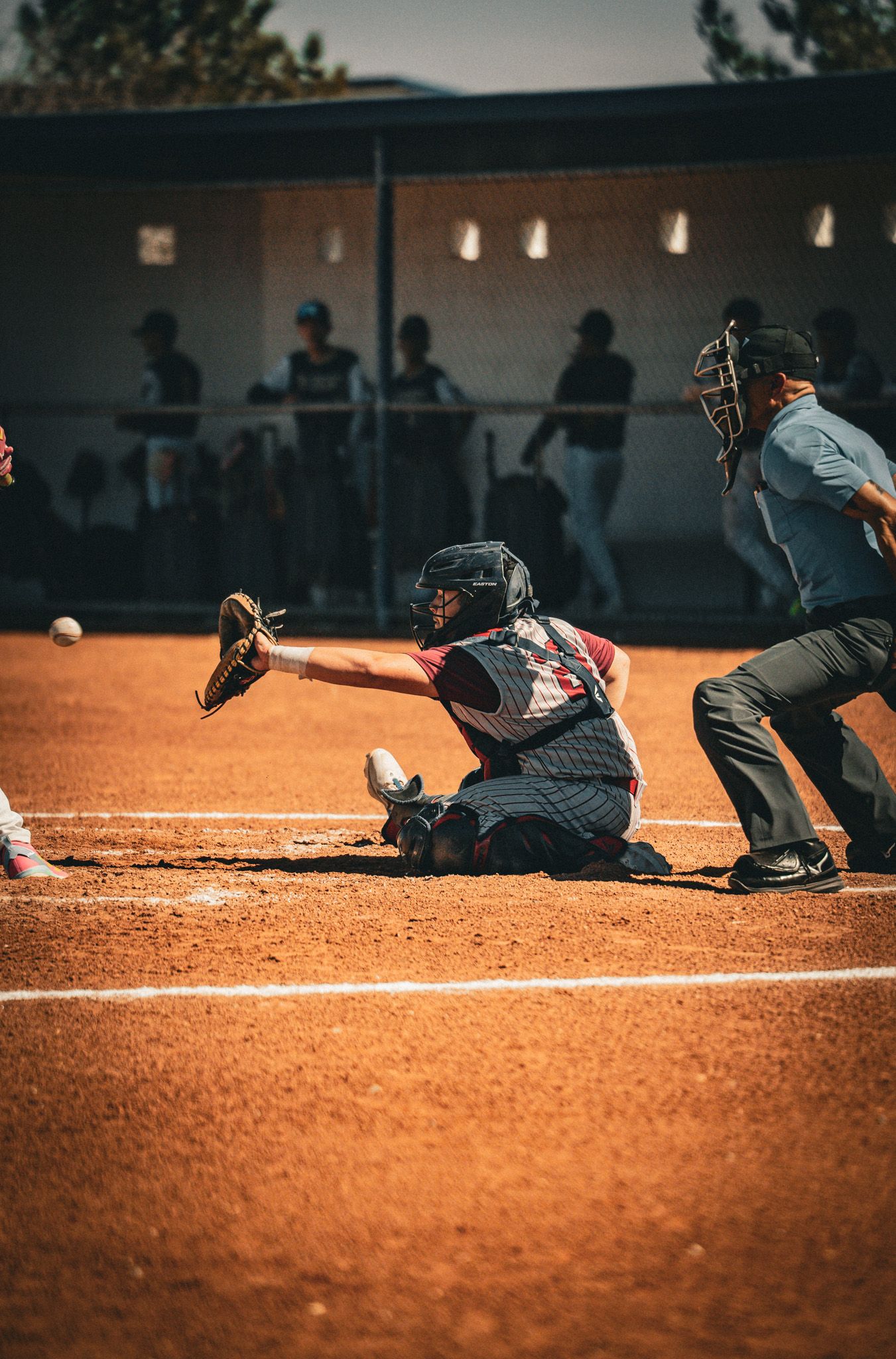 Baseball players in action during a game with catcher and batter on a dusty orange clay baseball field at dusk.