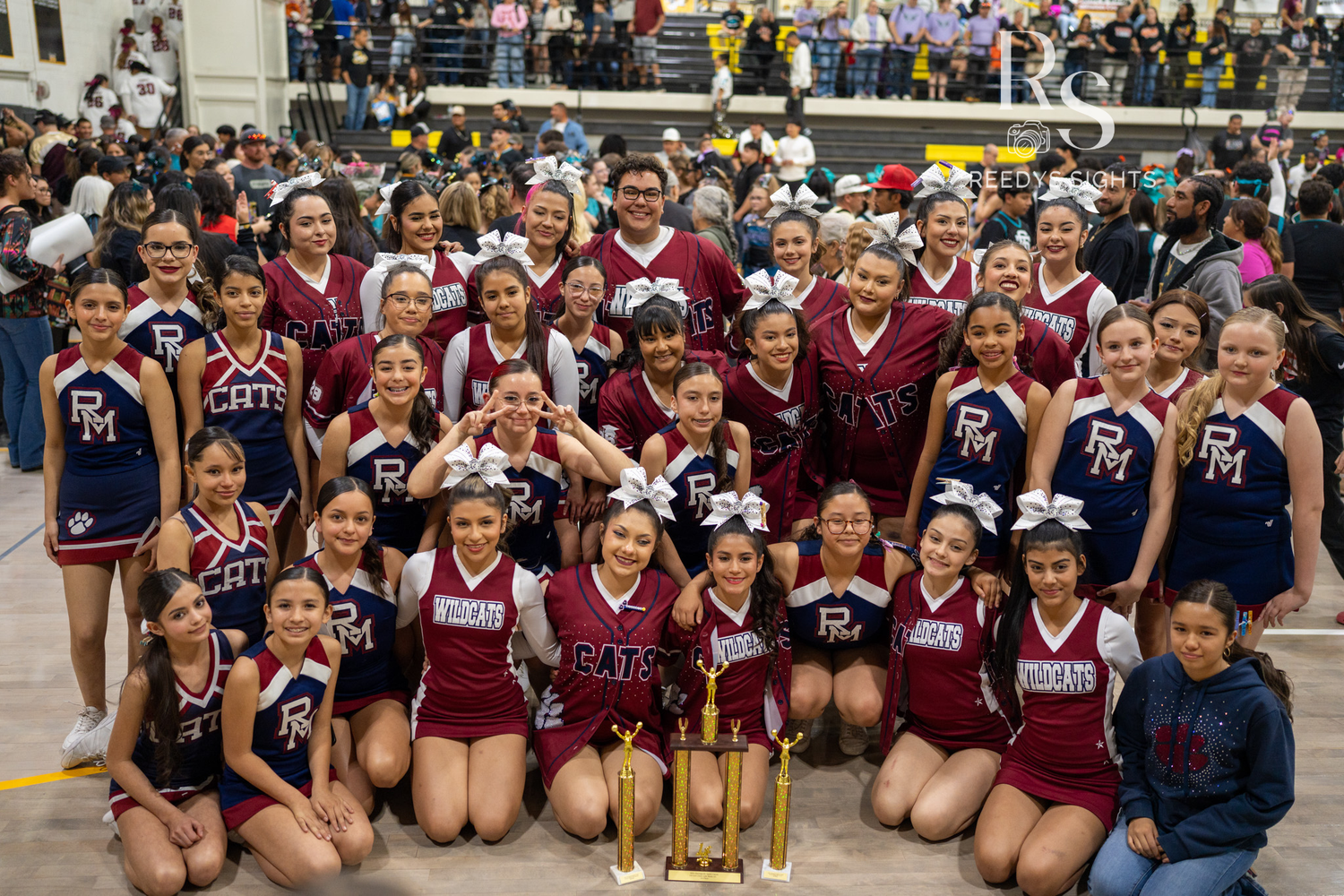 Two cheerleading teams in maroon and navy uniforms pose together with a trophy after a competition.