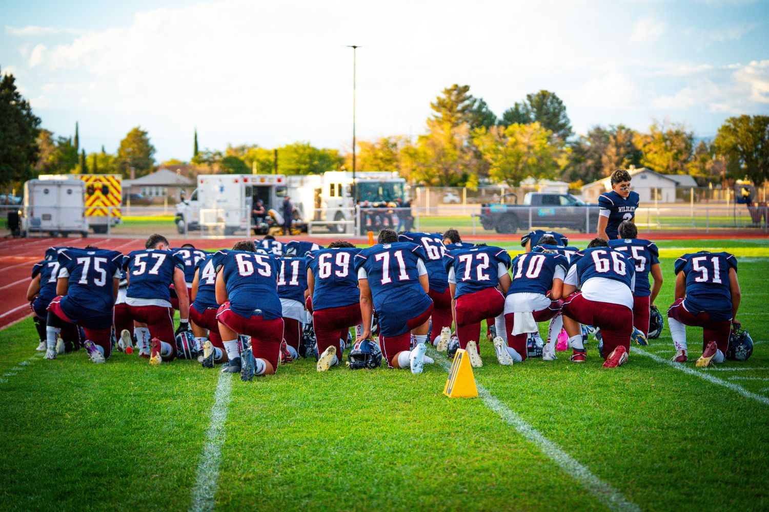 Football players line up on a sunny field during a game with spectators watching from the sidelines.