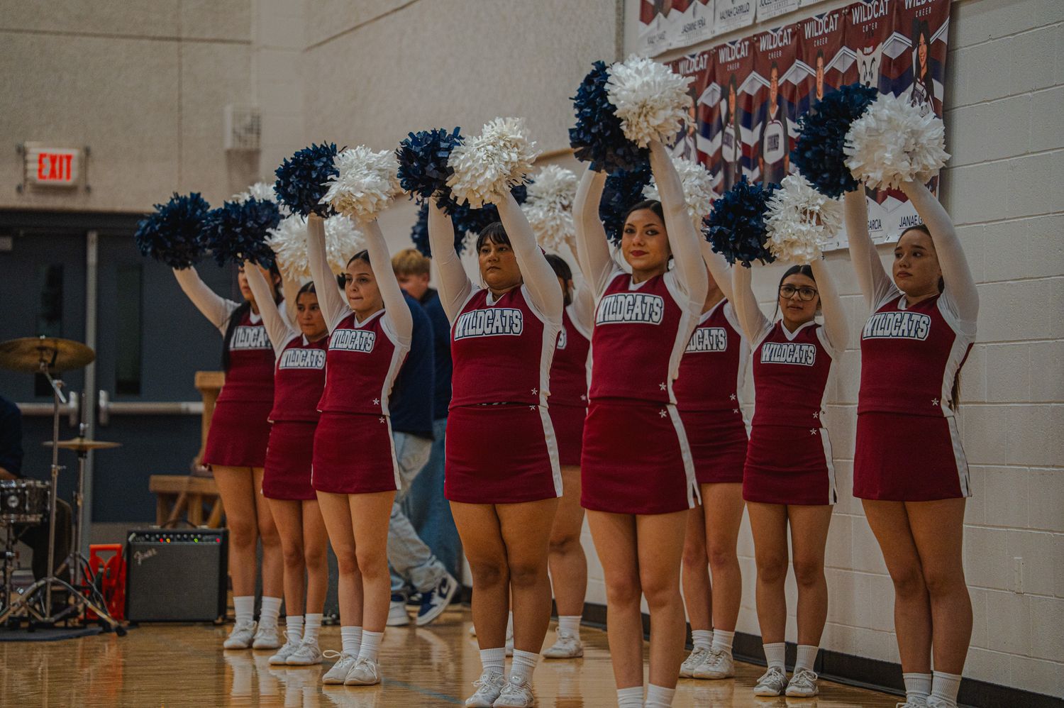 Cheerleaders in red uniforms performing with pom poms during indoor event.