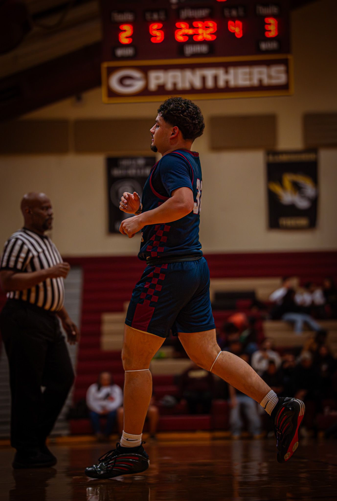 Basketball player dribbles down the court during an intense game with Panthers scoreboard visible in background.