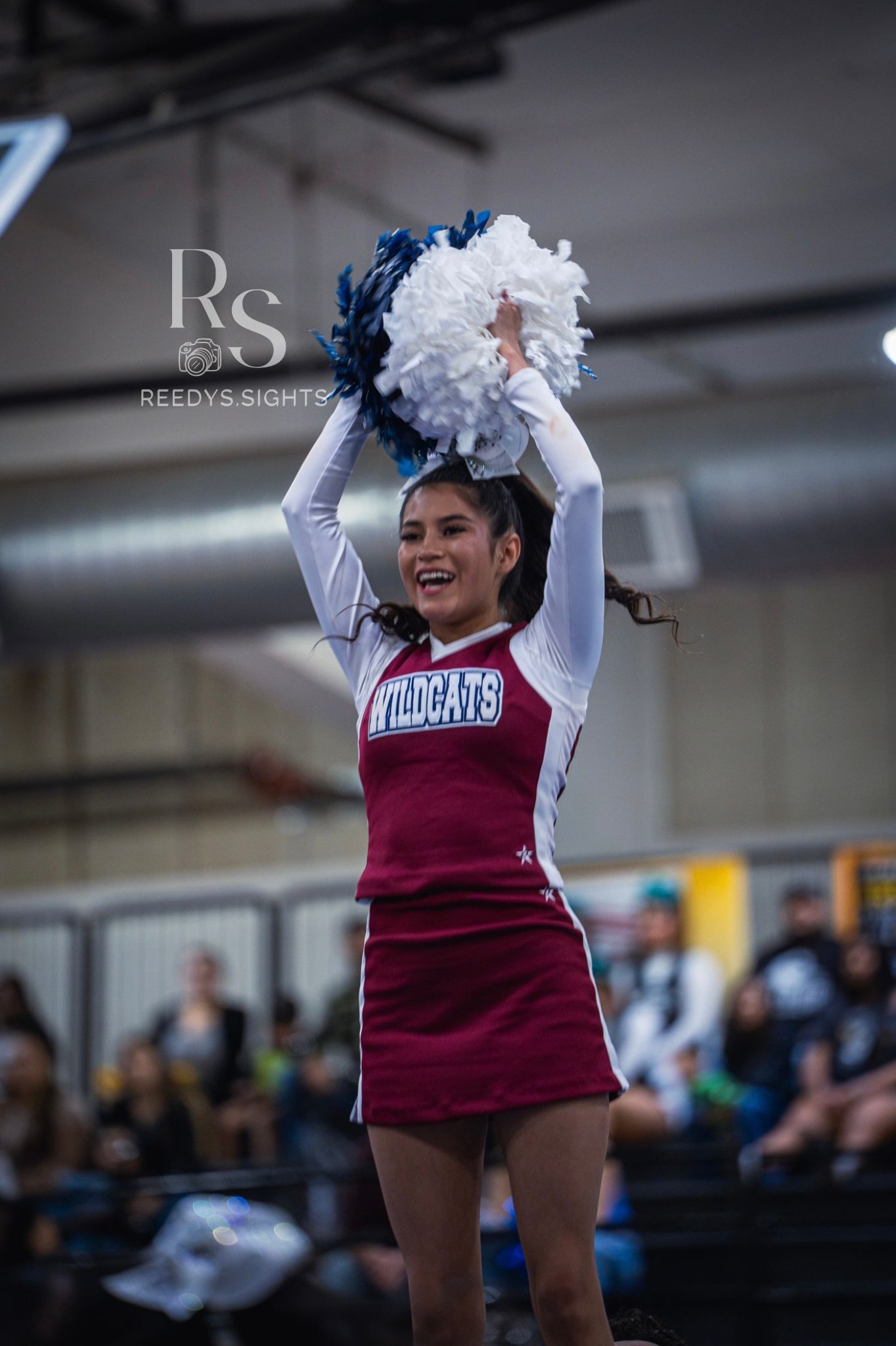 Cheerleaders in maroon and white uniforms raise pom poms during an indoor performance.