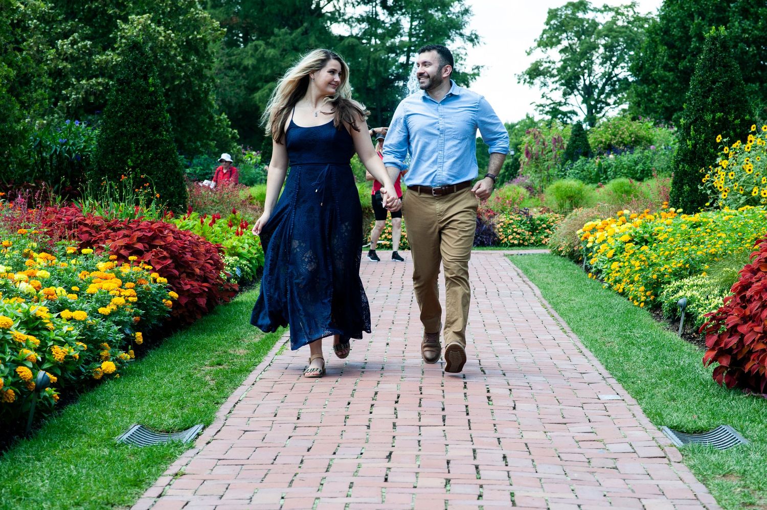 Engaged couple holds hands and runs down a path of colorful flowers at Longwood Gardens in Pennsylvania.
